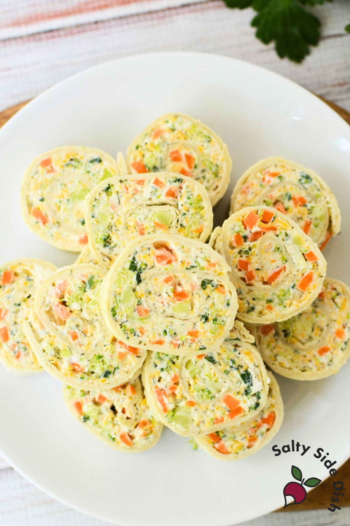 Soft tortilla being rolled up with creamy vegetable filling made from cream cheese, carrots, broccoli, and shredded cheese.