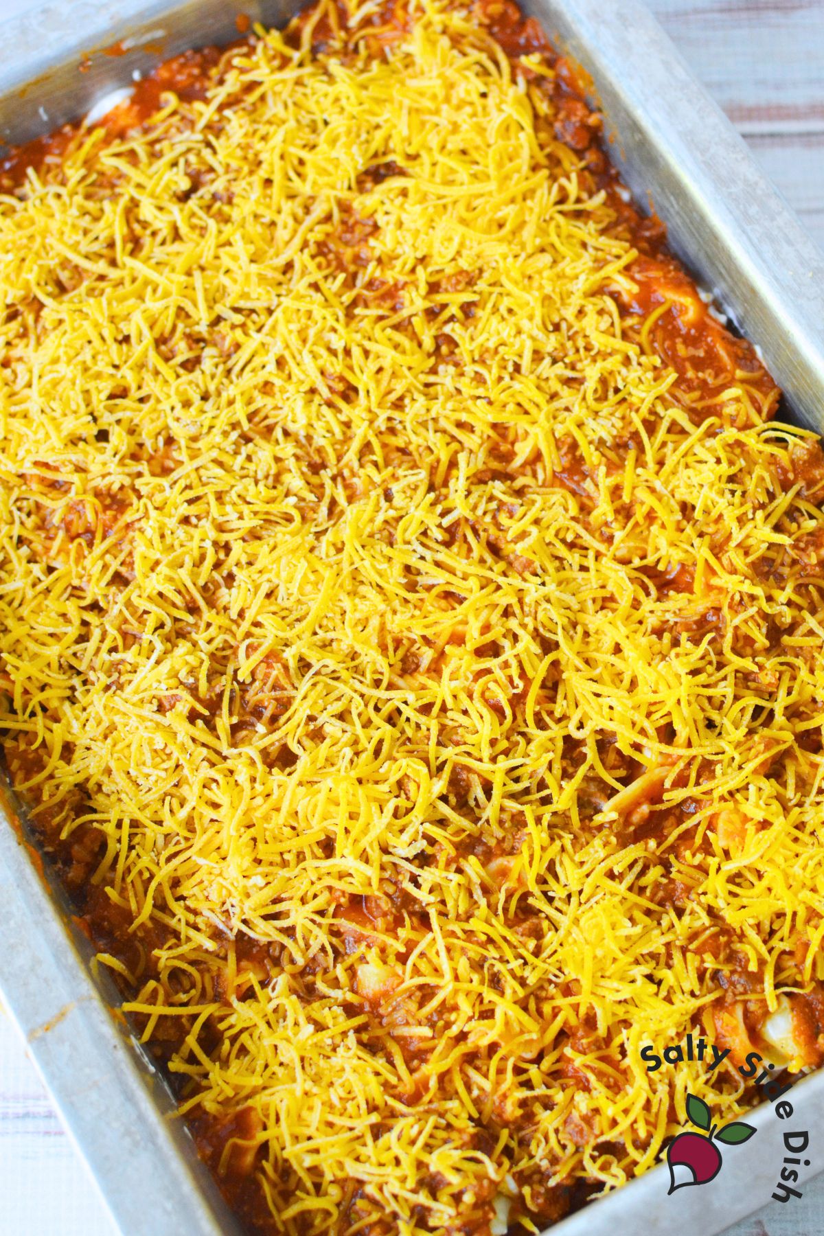 tomato beef noodle casserole topped with shredded cheddar before baking