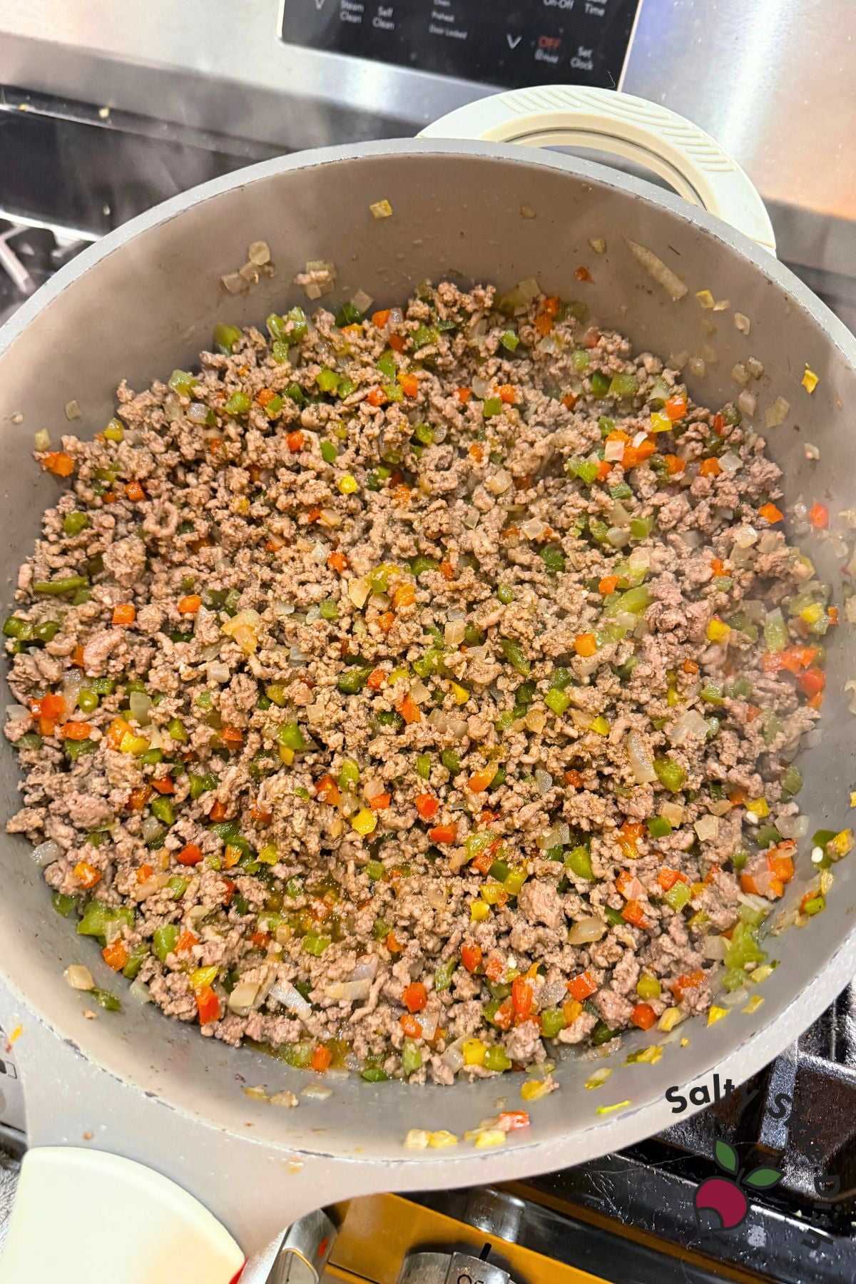 Large skillet with cooked ground beef, onions, and colorful diced bell peppers for rice bowls