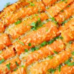 Oven baked garlic parmesan carrots on parchment with melted cheese and parsley — simple and delicious baked carrot recipe.