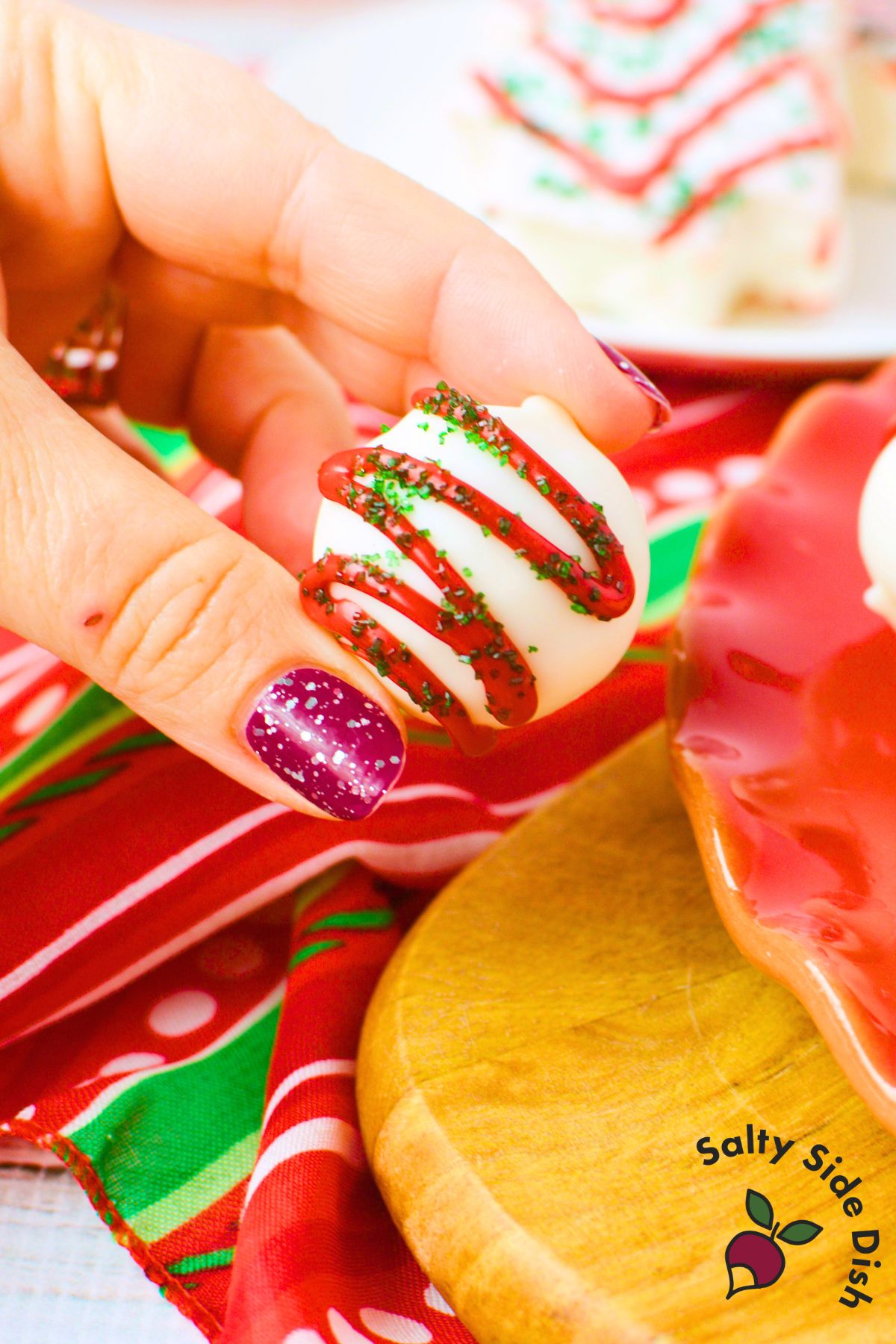 small christmas tree cake truffle with white chocolate shell and red drizzle held in hand for serving