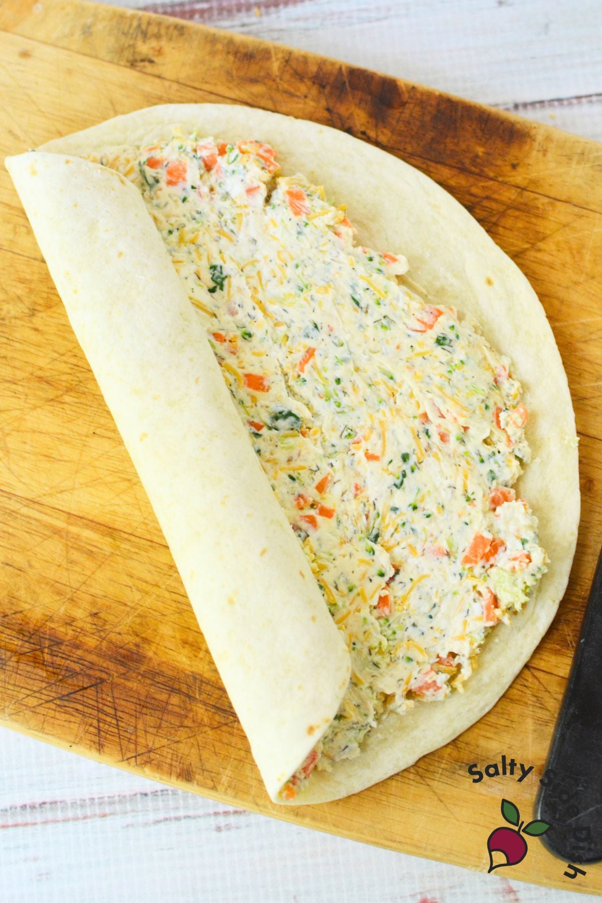 Close-up of veggie pinwheels sliced and stacked on a plate, showing colorful layers of carrots, broccoli, and creamy filling.