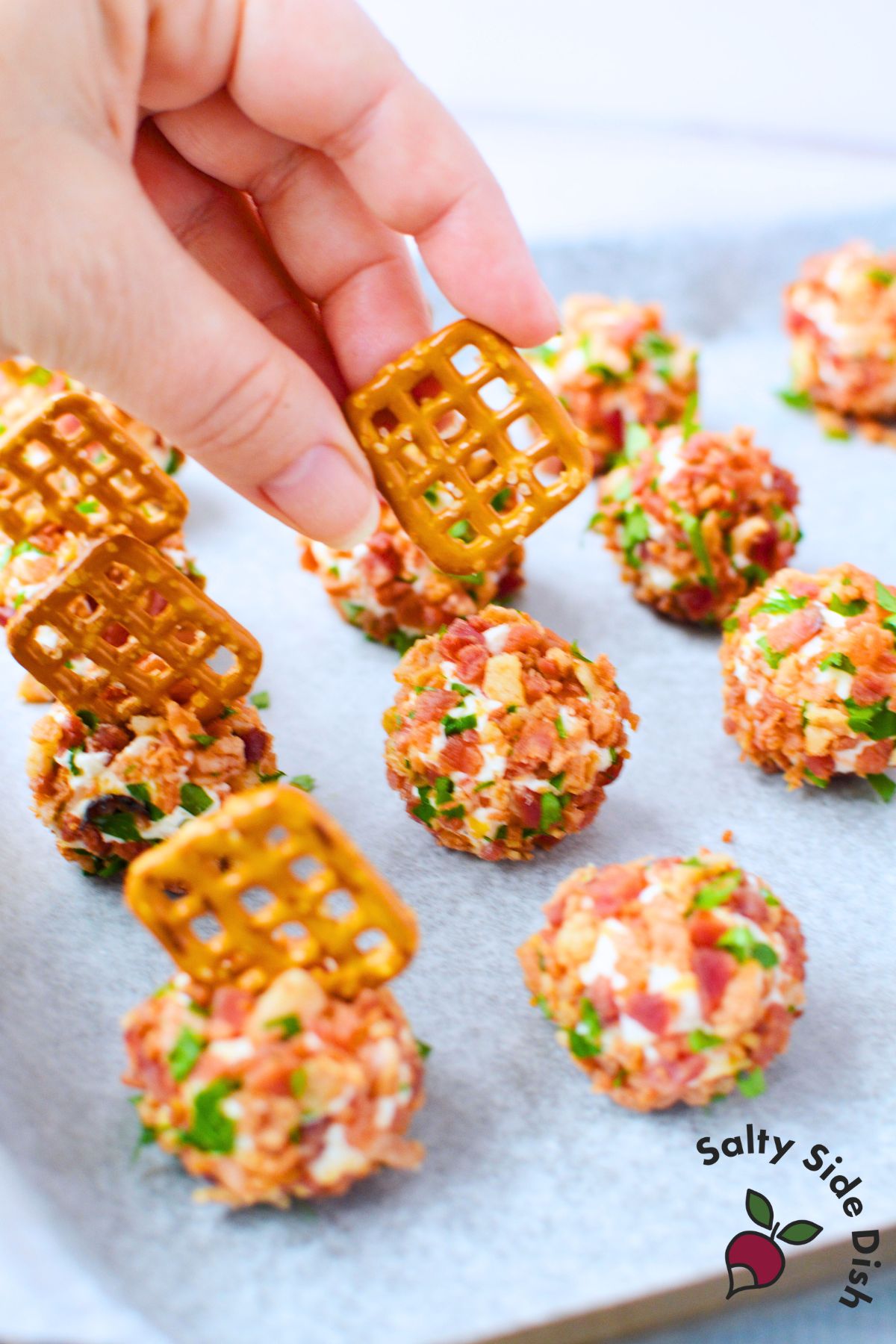 Pretzel-topped mini cheese balls with creamy bacon ranch filling, ready to serve on a parchment-lined tray for a quick crowd-pleasing snack.
