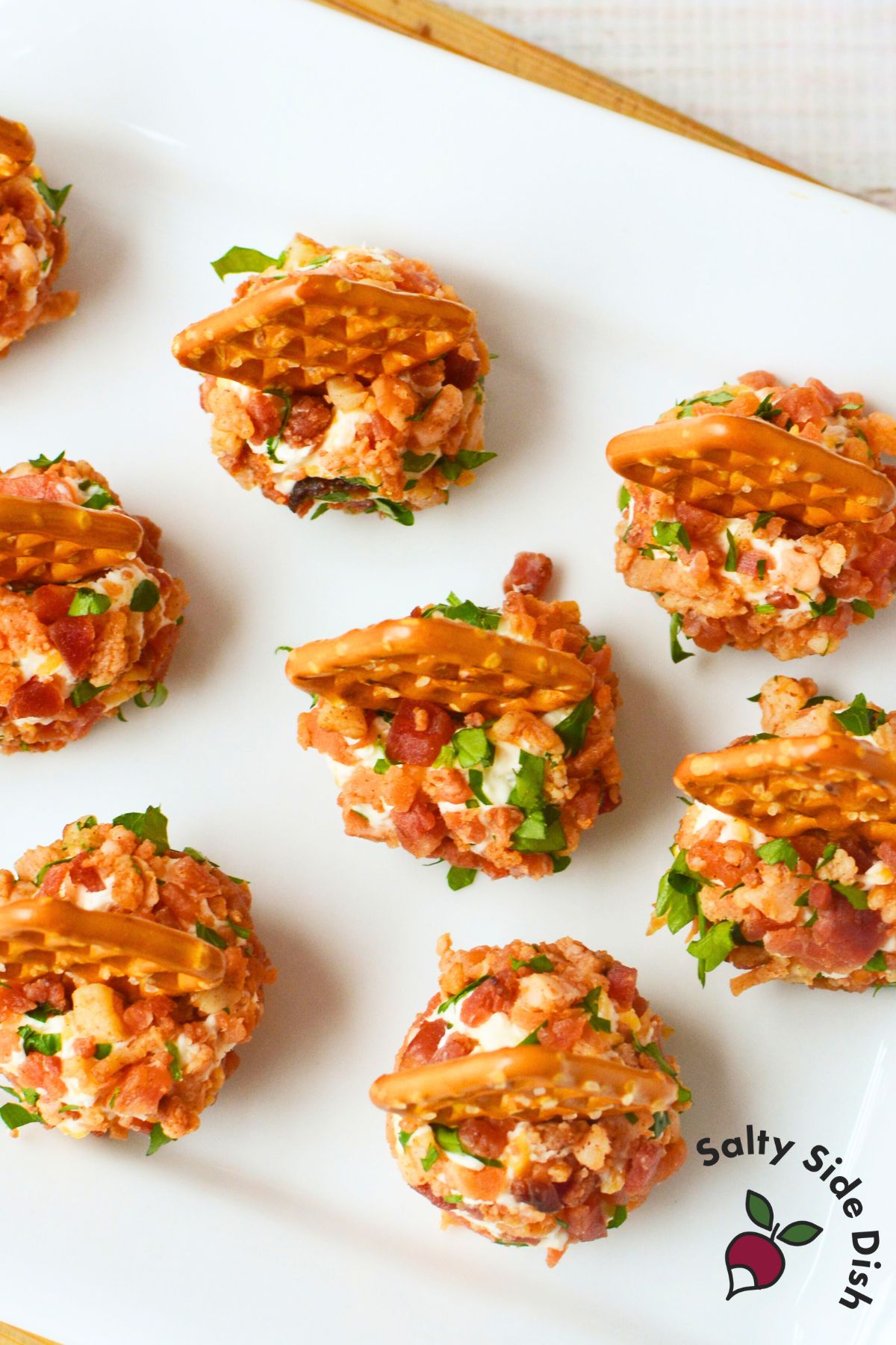 Hand placing pretzel squares into mini bacon ranch cheeseballs on parchment paper, showing the easy assembly of this holiday appetizer.