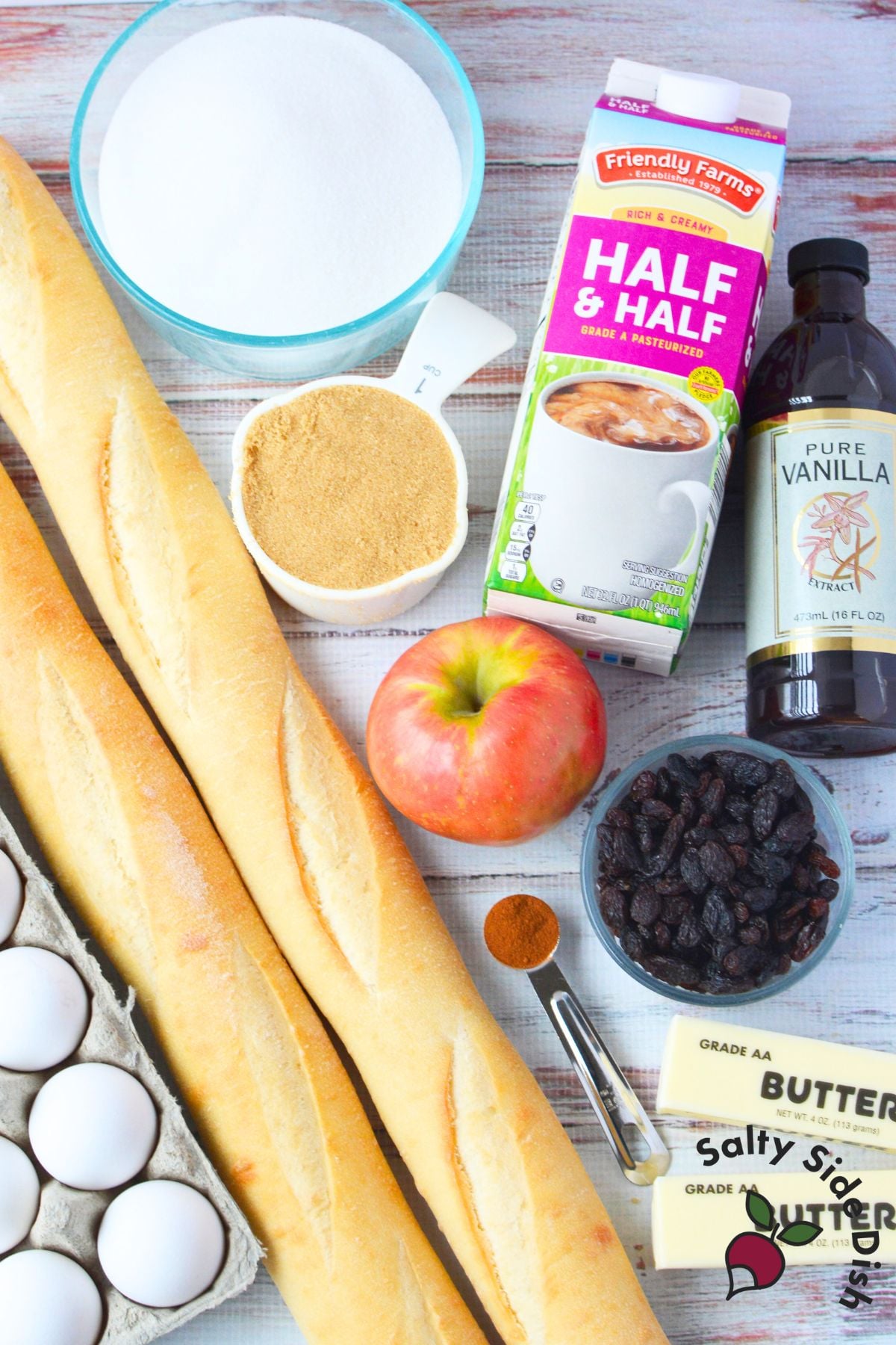 bread pudding ingredients laid out including baguettes eggs sugars half and half apples and raisins