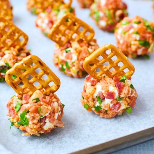 Mini cheeseball bites on a white serving platter with pretzels inserted, showing a simple cream cheese, bacon, and ranch appetizer recipe.