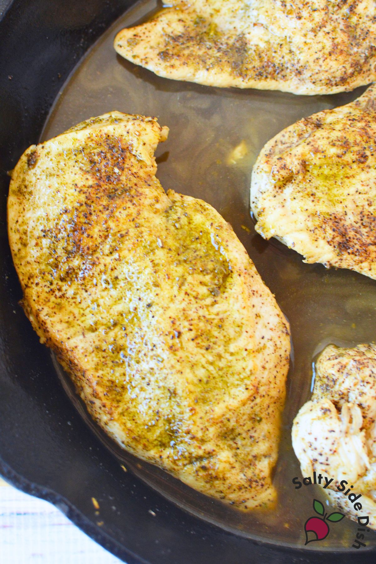 Juicy chicken breasts cooking in a hot cast iron skillet with light oil and seasoning.