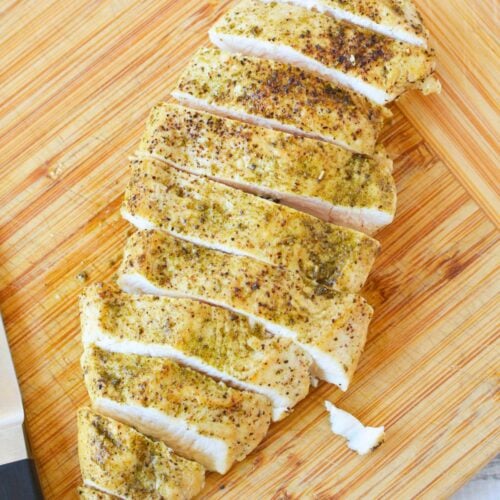 Juicy sliced chicken breast on a wooden cutting board after cooking in a cast iron skillet.