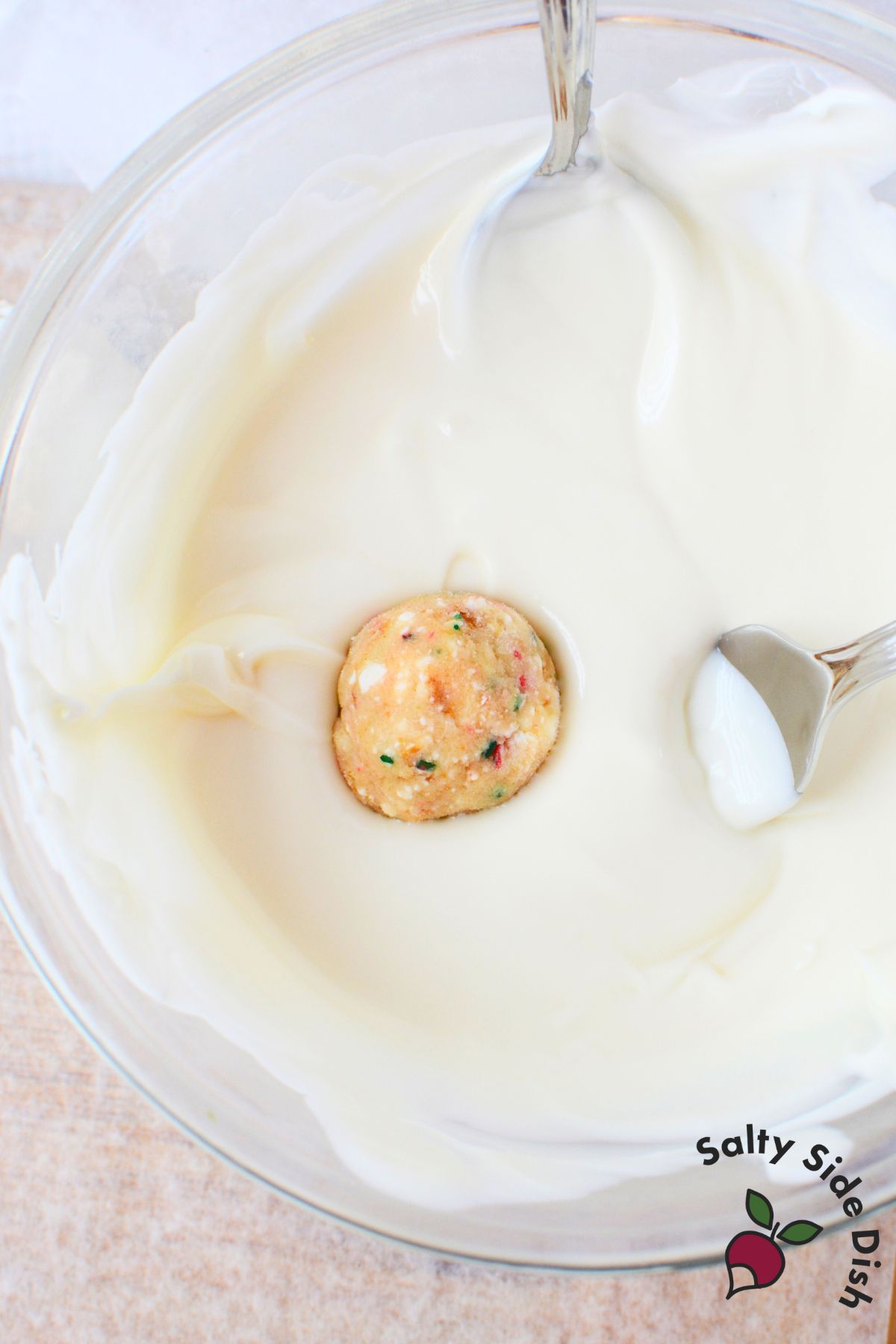 christmas tree cake truffle ball being dipped into melted vanilla almond bark for coating