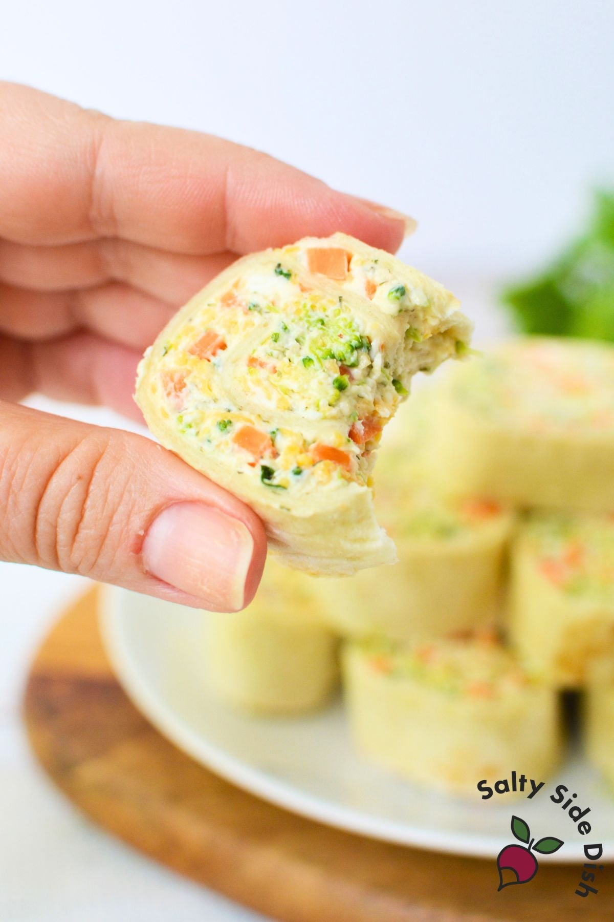 Colorful veggie pinwheels made with cream cheese, shredded carrots, broccoli, and cheddar rolled in soft tortillas on a white plate.