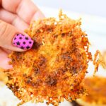 Hand holding a crispy baked TikTok onion ring with melted Parmesan cheese and golden brown edges