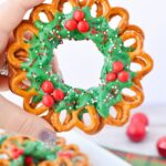 Chocolate pretzel wreath decorated with green candy coating, red cinnamon candies, and holiday sprinkles
