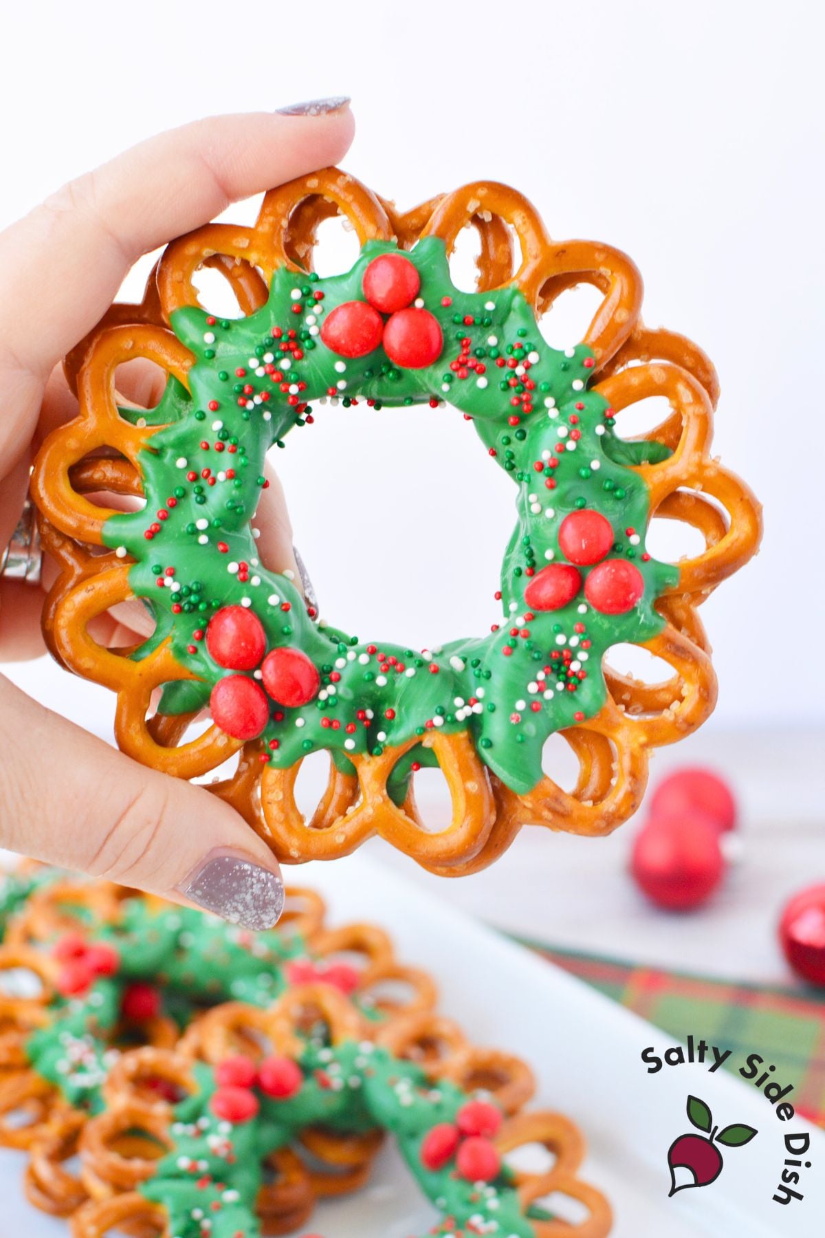 Chocolate pretzel wreath decorated with green candy coating, red cinnamon candies, and holiday sprinkles