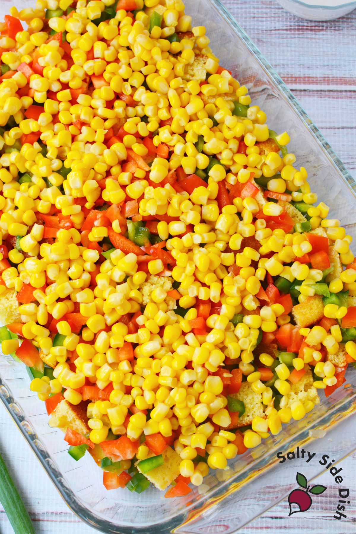 layered cornbread salad in a glass baking dish with corn bell peppers and tomatoes