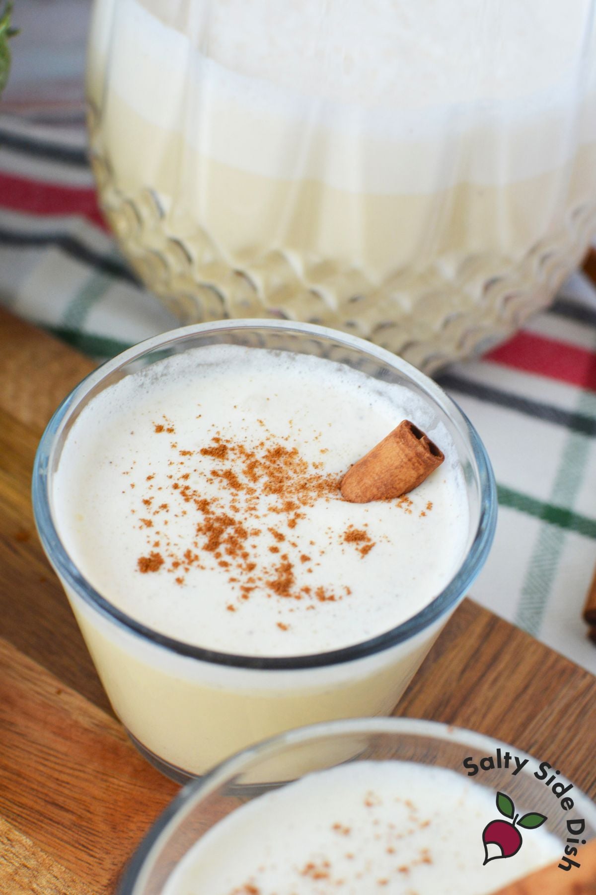 Close up of spiked eggnog in a clear glass with cinnamon garnish for Christmas eggnog serving