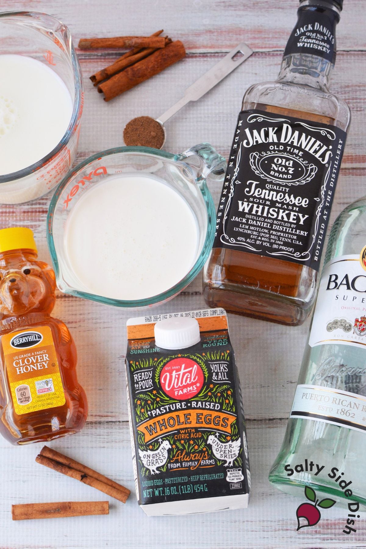 Ingredients for spiked eggnog including pasteurized whole eggs, milk, cream, honey, bourbon, rum, and nutmeg