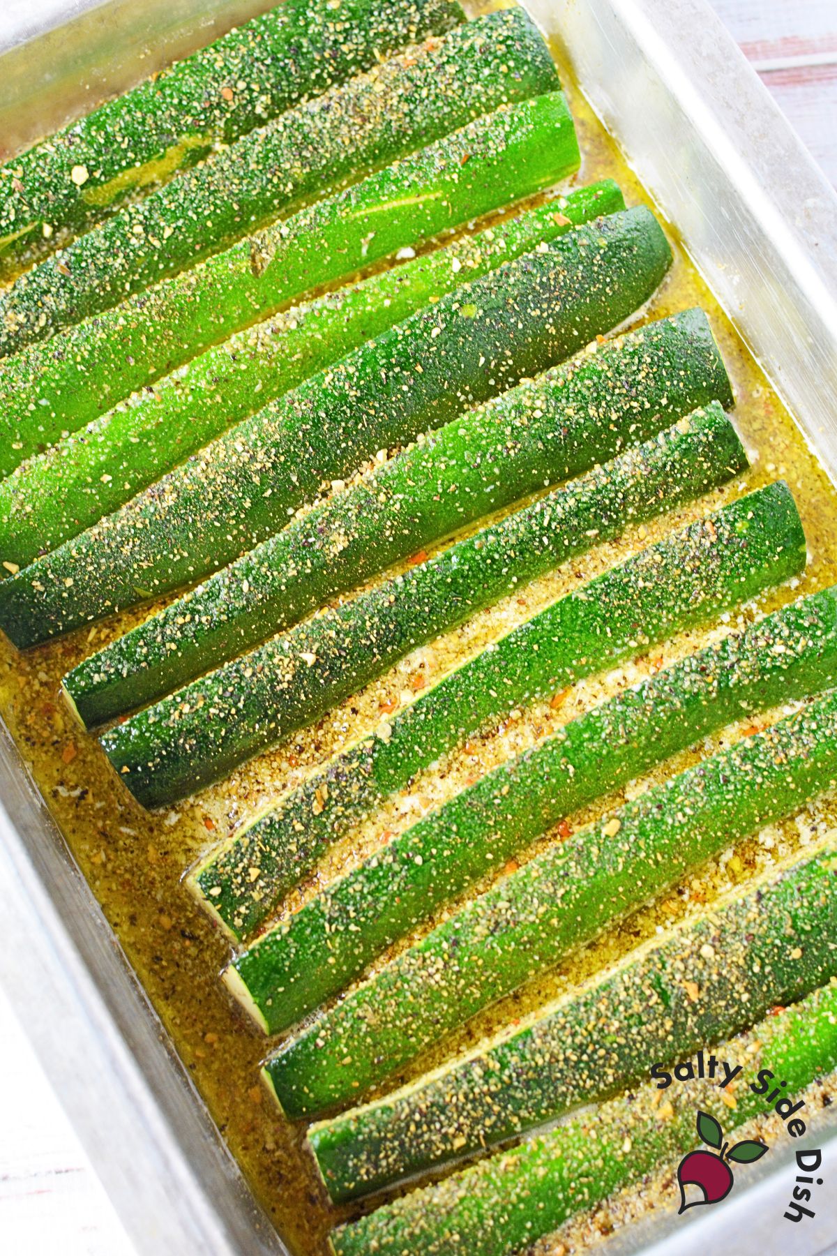 Zucchini spears arranged skin side up in melted butter and seasoning before oven roasting