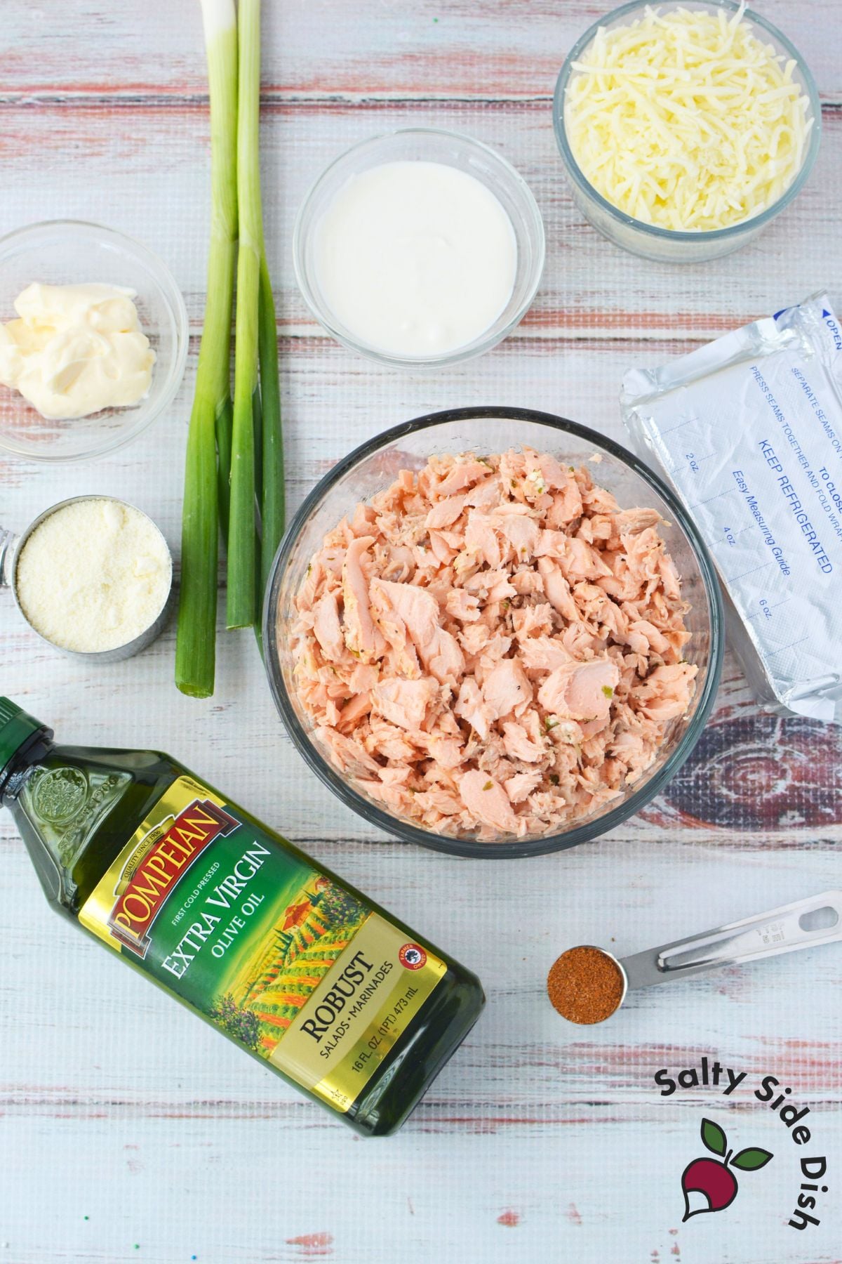 Ingredients for baked salmon dip including cooked salmon, cream cheese, sour cream, mayonnaise, mozzarella cheese, green onions, and Old Bay seasoning
