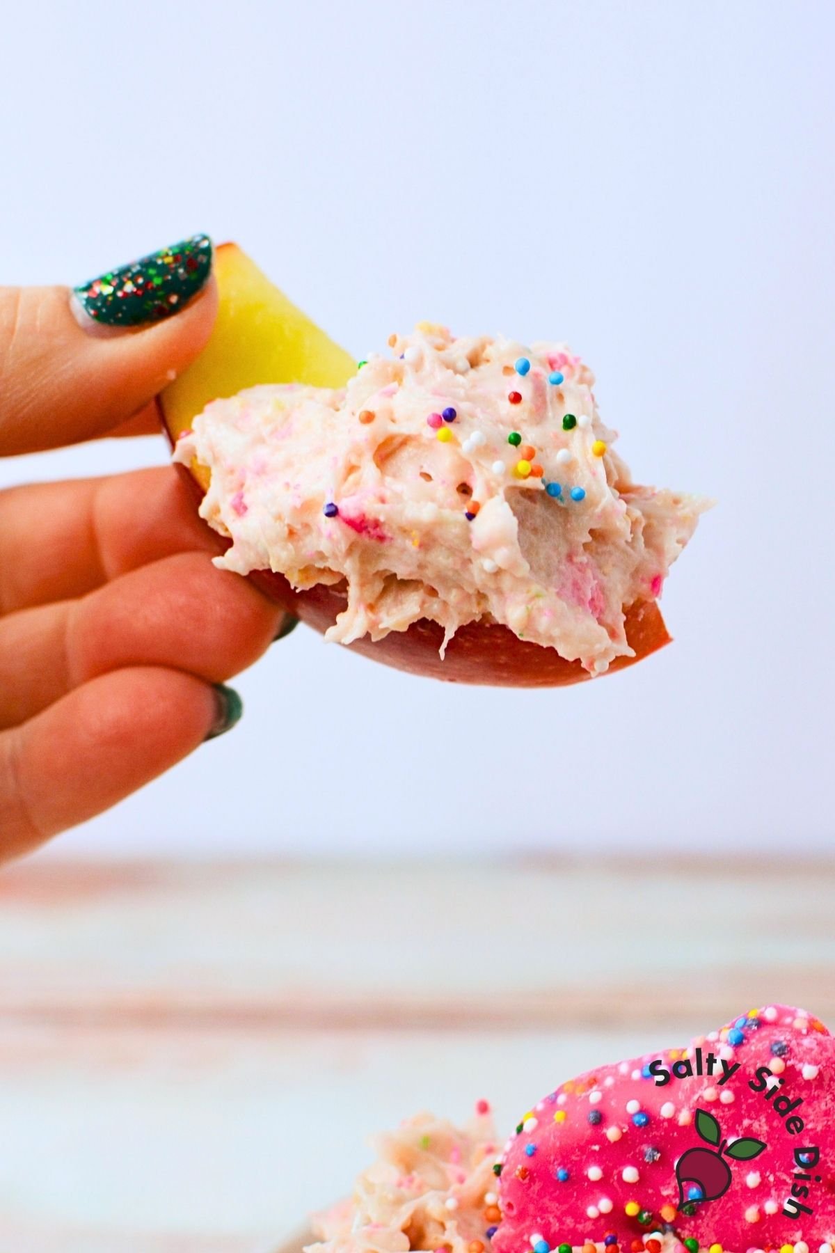 Apple slice dipped into creamy frosted animal cracker dessert dip