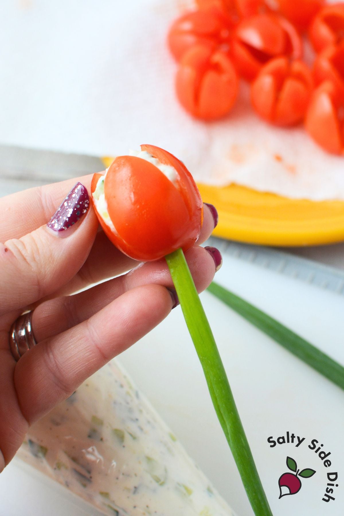 Tulip tomato appetizer made from a stuffed cherry tomato filled with cream cheese and cucumber and finished with a green onion stem