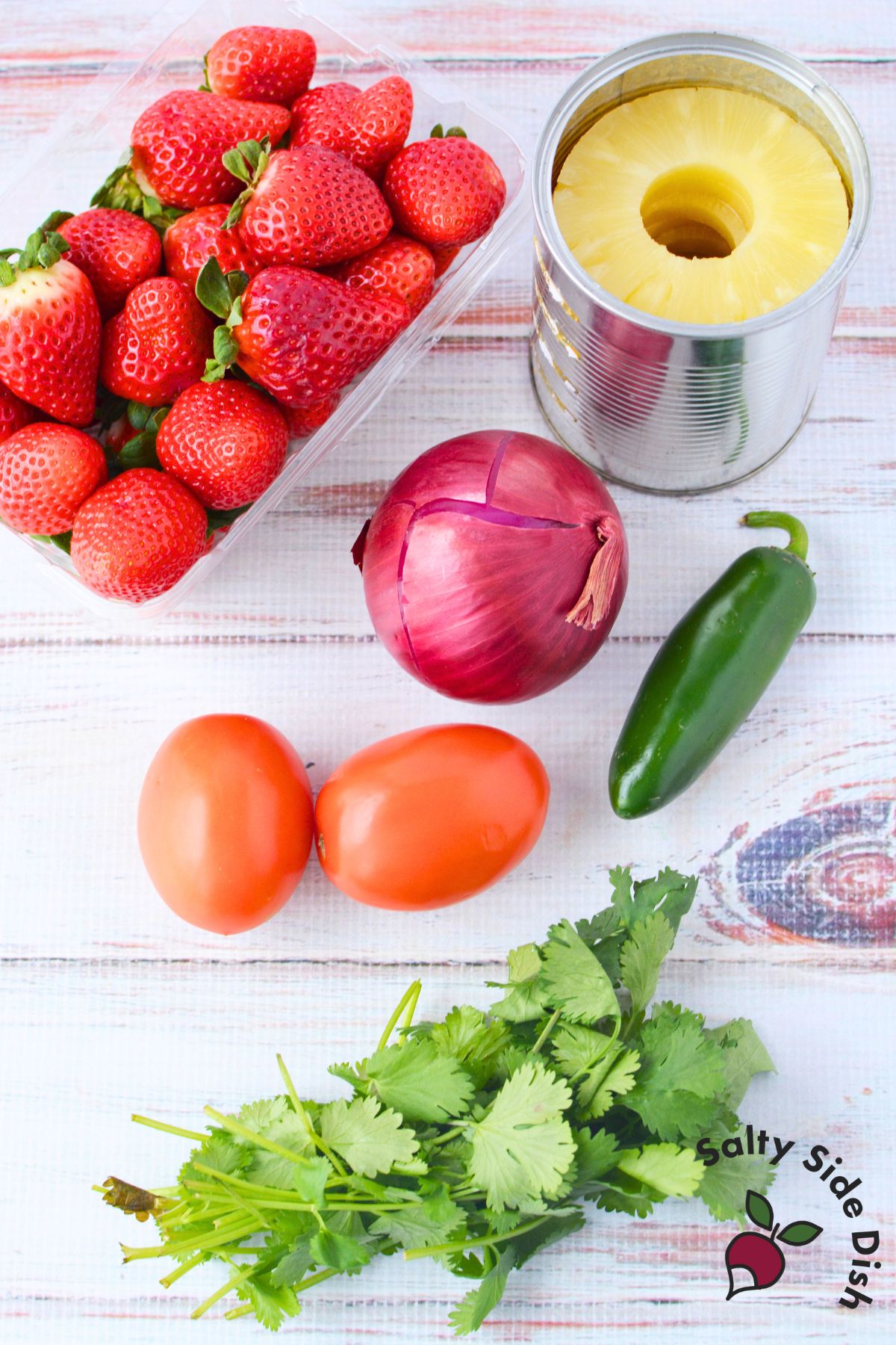 Ingredients for strawberry pineapple salsa including strawberries, pineapple, tomatoes, red onion, jalapeno, and cilantro