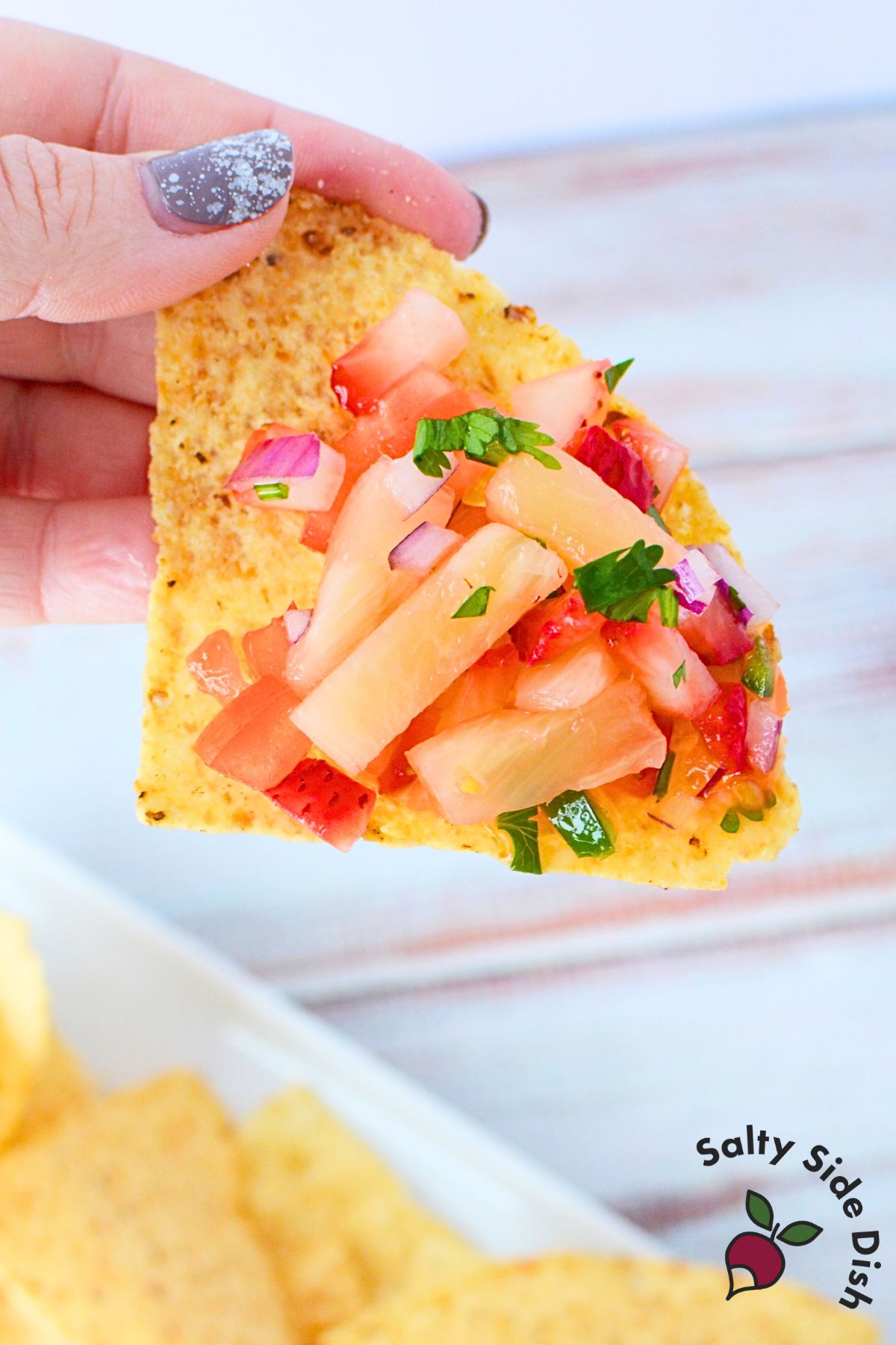 Chopped strawberries, pineapple, tomatoes, onion, jalapeno, and cilantro in a mixing bowl before mixing