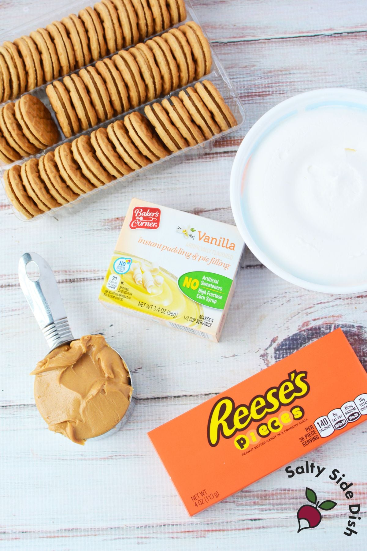 Ingredients for peanut butter icebox cake including peanut butter cookies, vanilla pudding, whipped topping, milk, and Reese’s Pieces