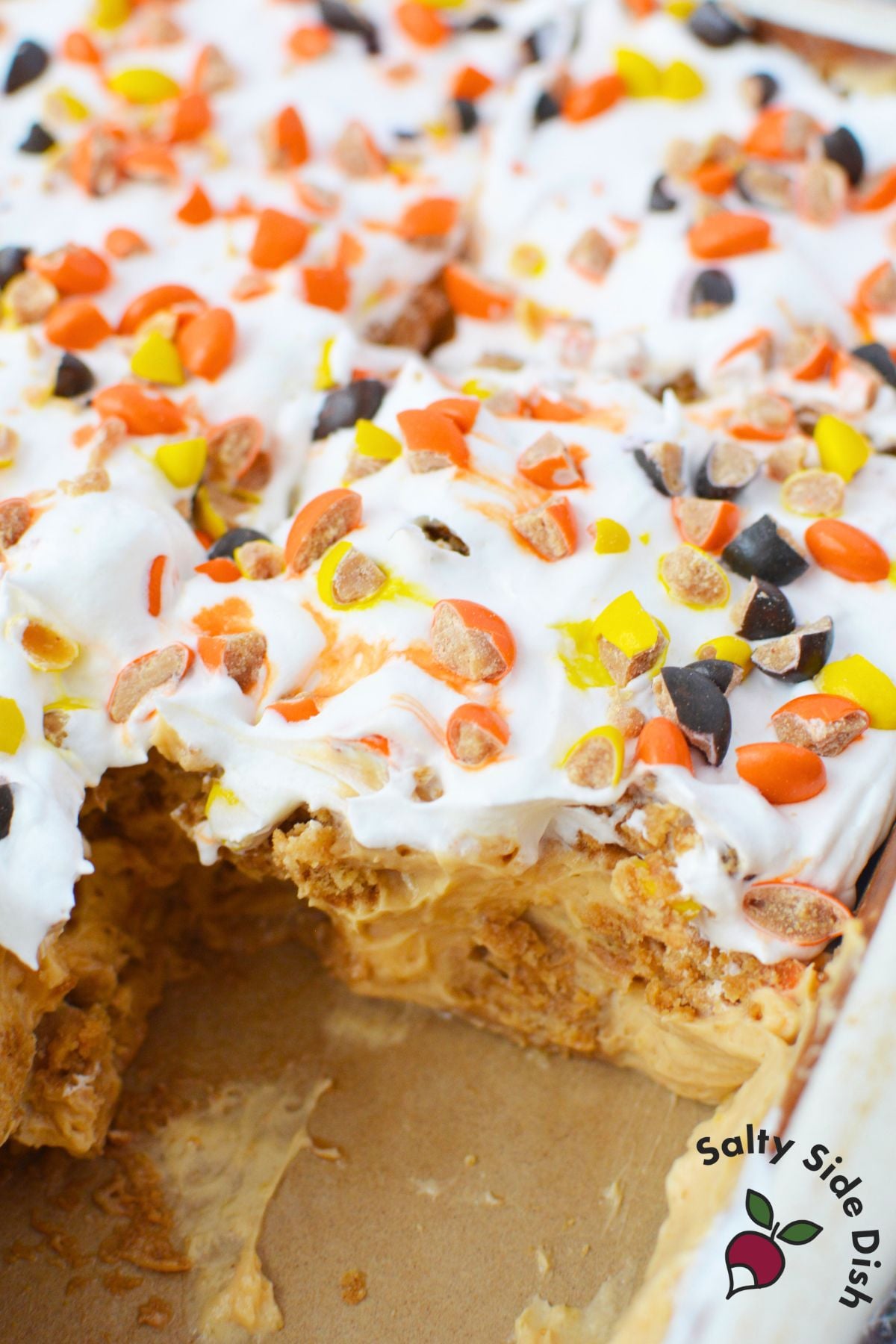 Peanut butter icebox cake topped with whipped topping and chopped Reese’s Pieces in a baking dish