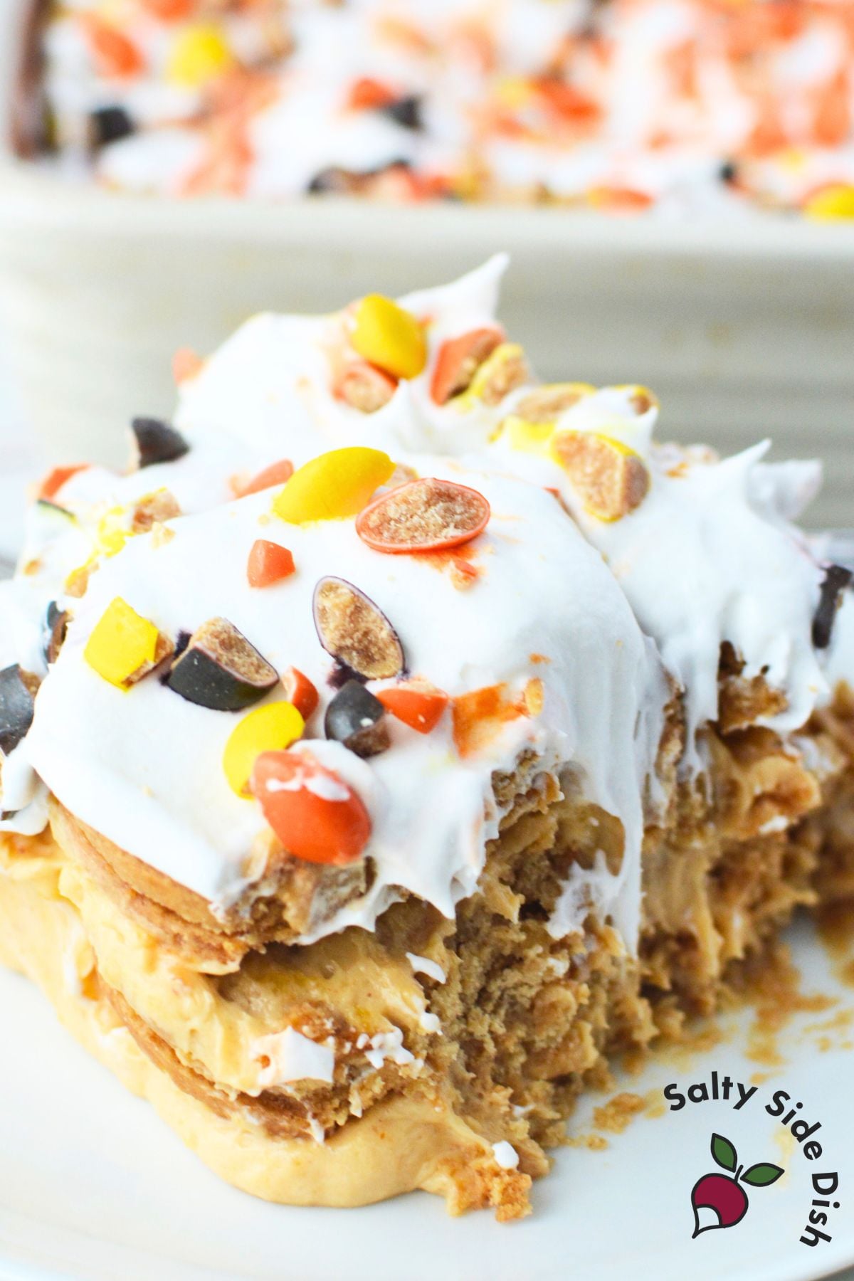 Chopped Reese’s Pieces sprinkled over whipped topping on peanut butter icebox cake