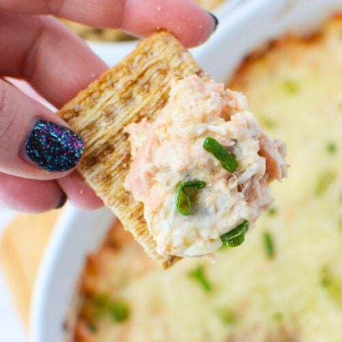 Cracker dipped into warm baked salmon dip with melted cheese and green onions