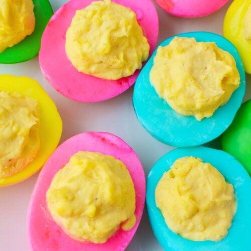 finished colored deviled eggs with bright pink yellow and green egg whites on a serving tray