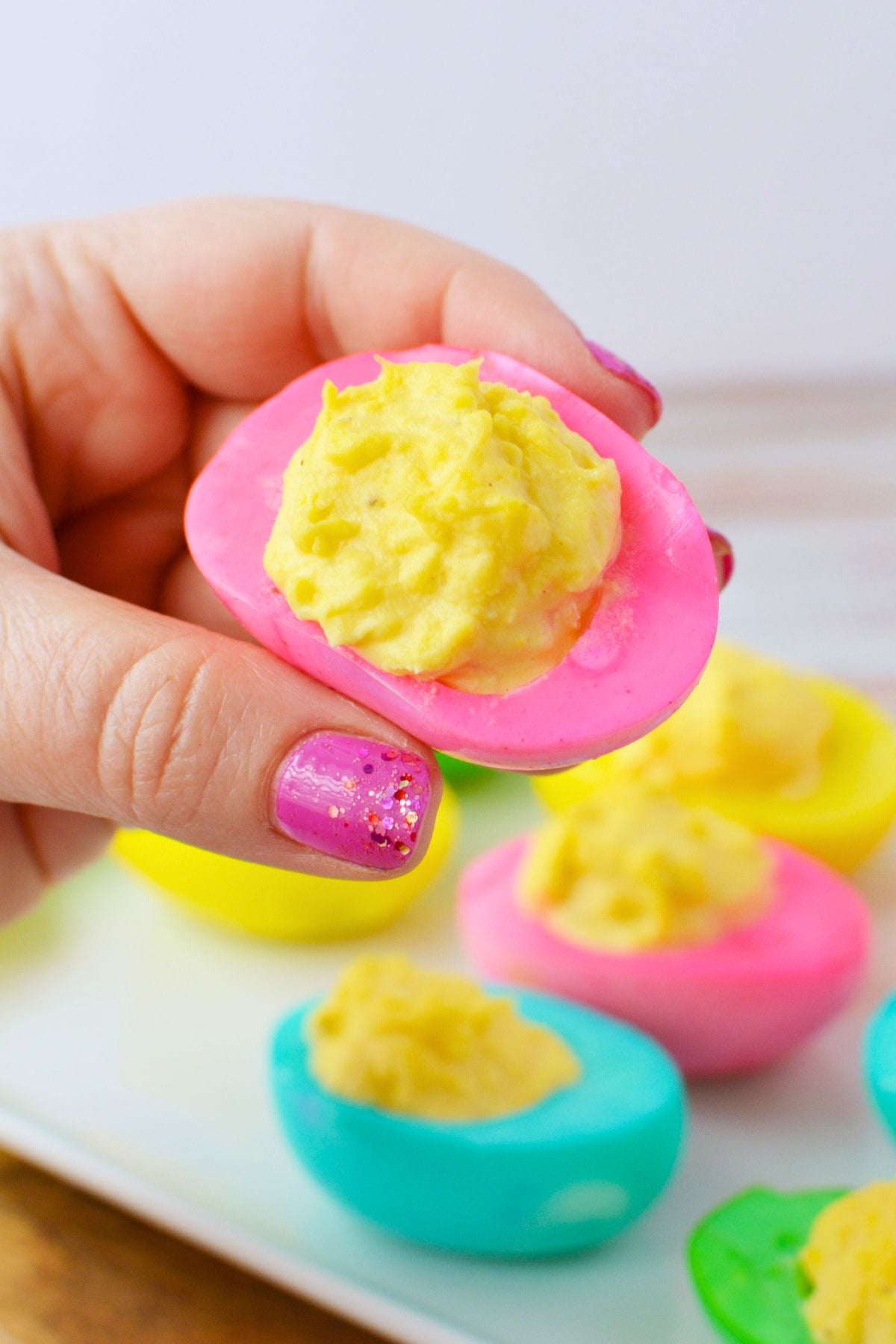 hand holding a pink colored deviled egg filled with smooth deviled egg filling