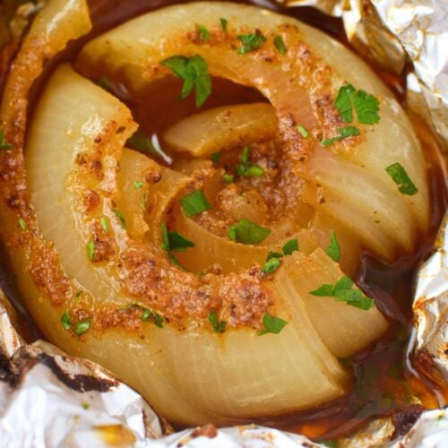 Close up of a baked onion boil split open showing soft buttery layers with Old Bay seasoning and parsley in a pool of rich juices