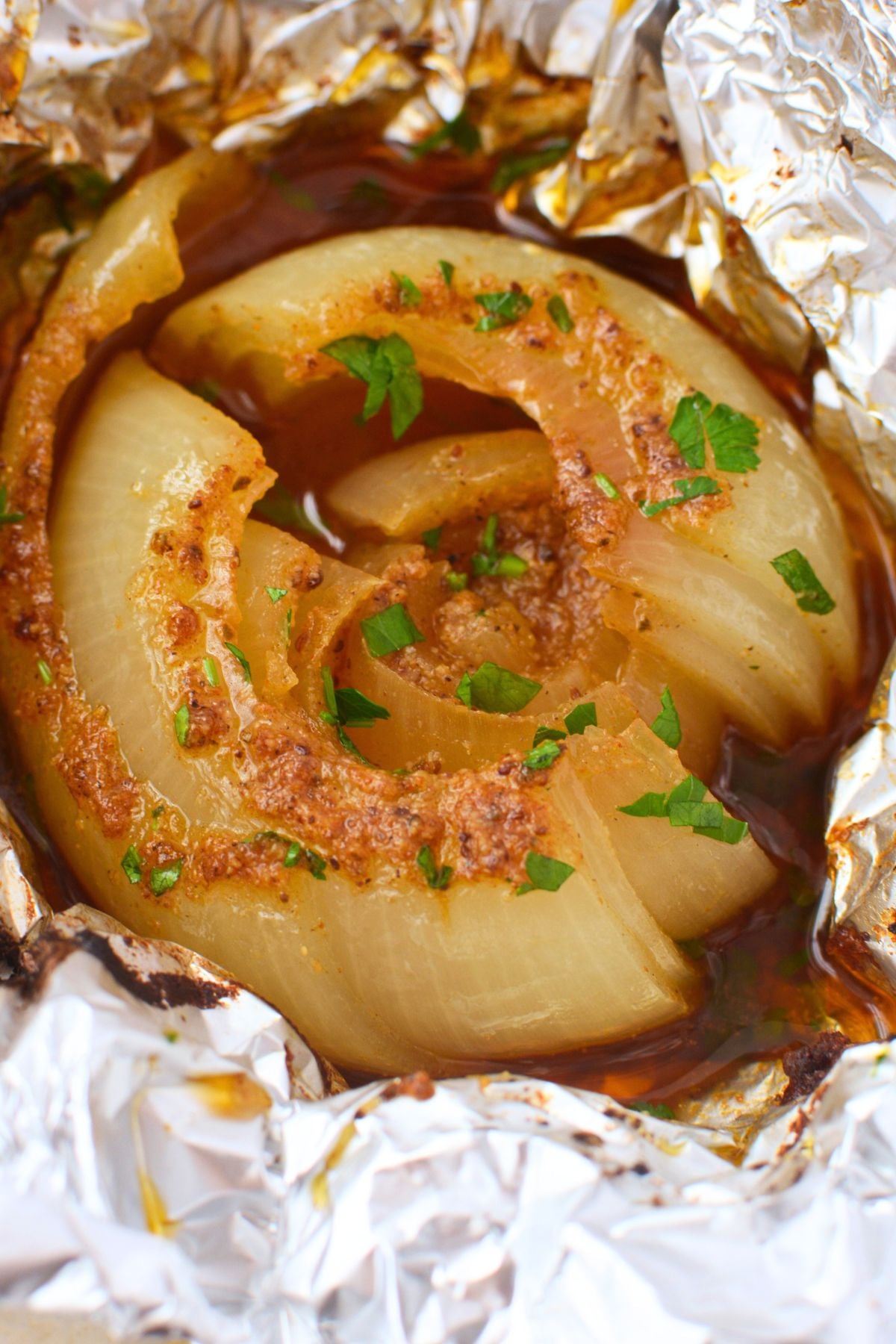 Close up of a baked onion boil split open showing soft buttery layers with Old Bay seasoning and parsley in a pool of rich juices