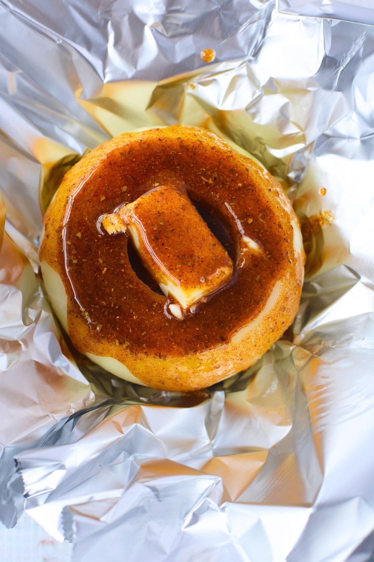 A cored sweet onion on foil topped with butter and drizzled with an Old Bay olive oil seasoning mixture