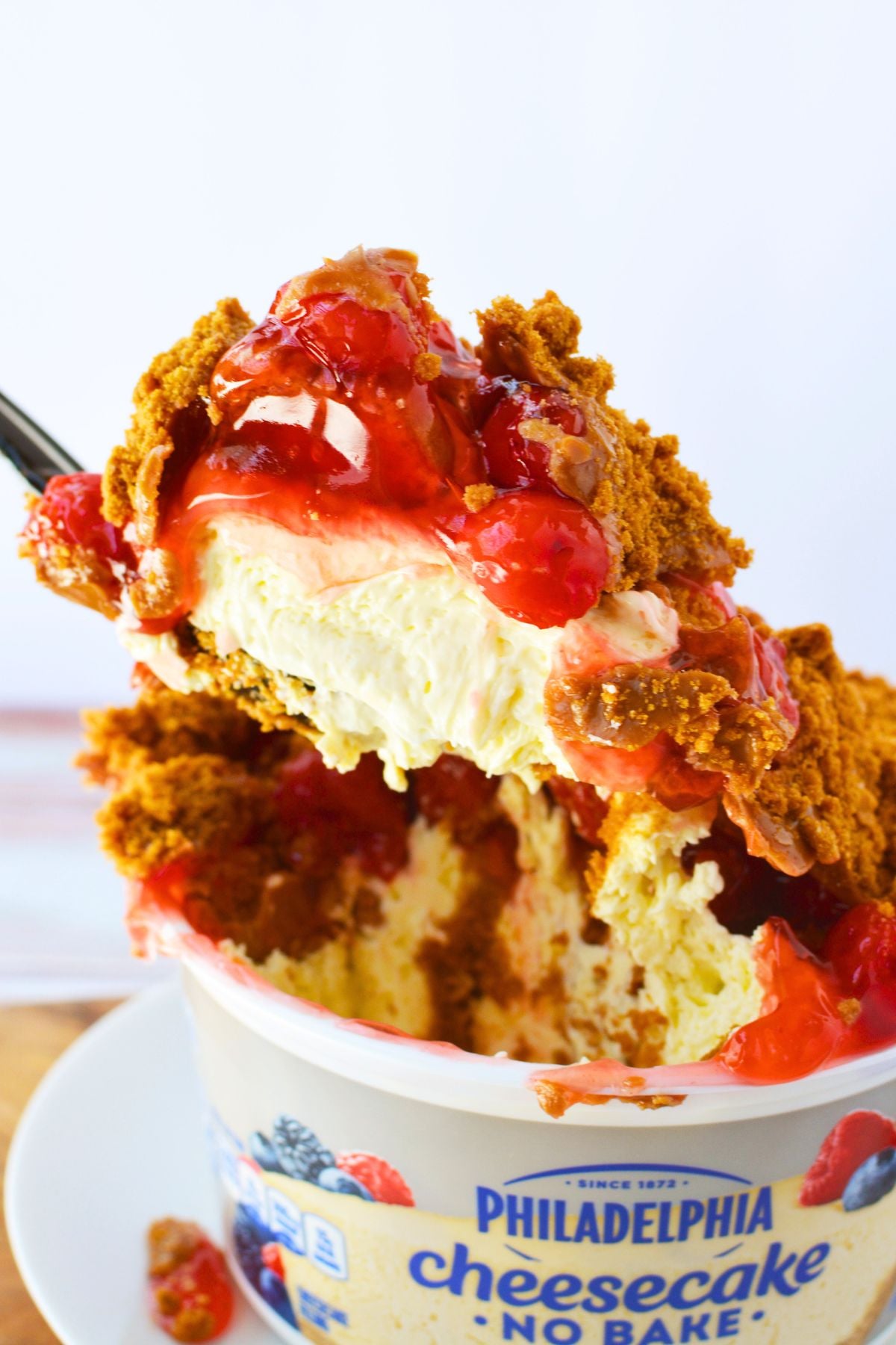 Close up scoop of no bake cheesecake topped with cherry pie filling, crushed Biscoff cookies, and cookie butter