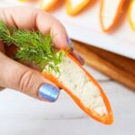 Row of stuffed mini pepper carrots filled with Boursin cheese and topped with fresh dill on a white rectangular platter