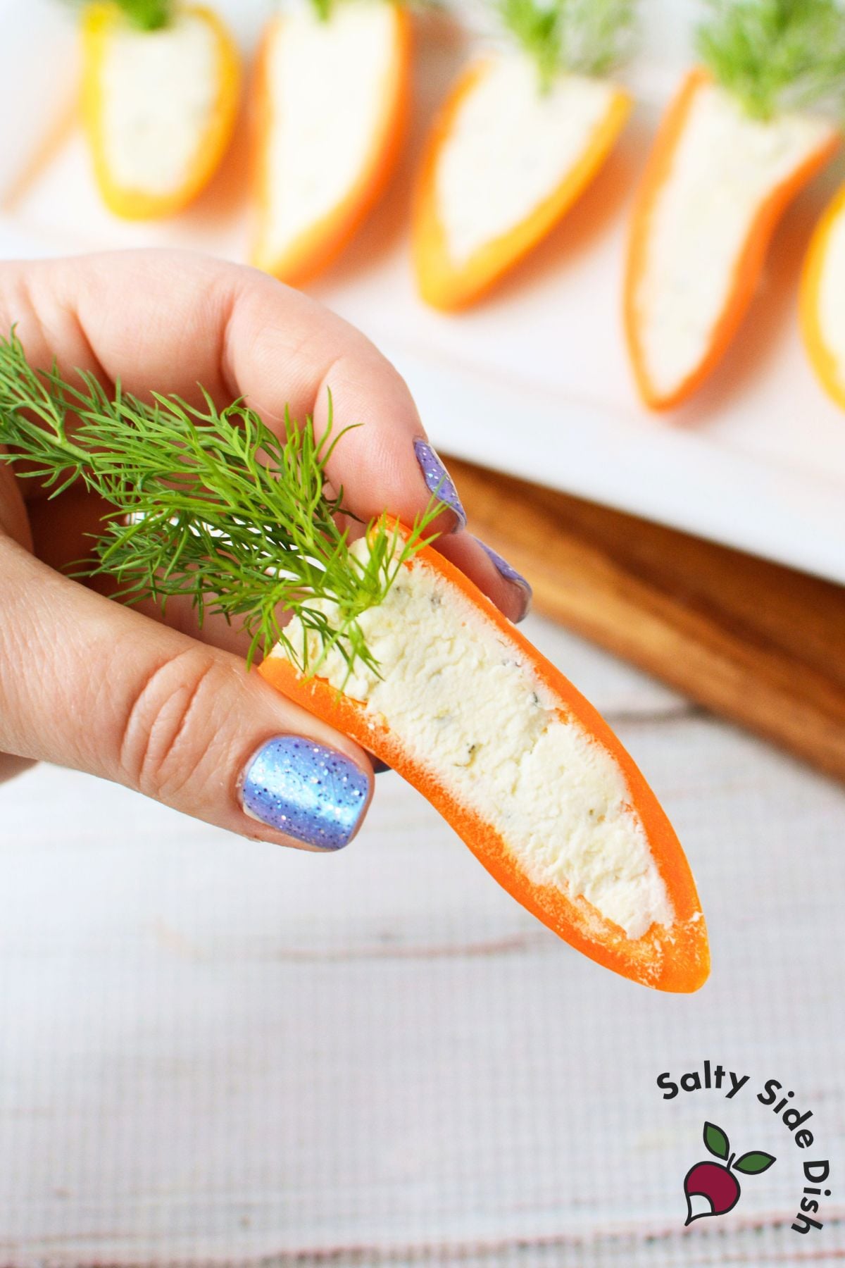 Row of stuffed mini pepper carrots filled with Boursin cheese and topped with fresh dill on a white rectangular platter