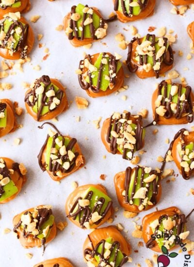 Overhead view of finished caramel apple pretzel bites with chocolate drizzle and chopped peanuts scattered across parchment paper
