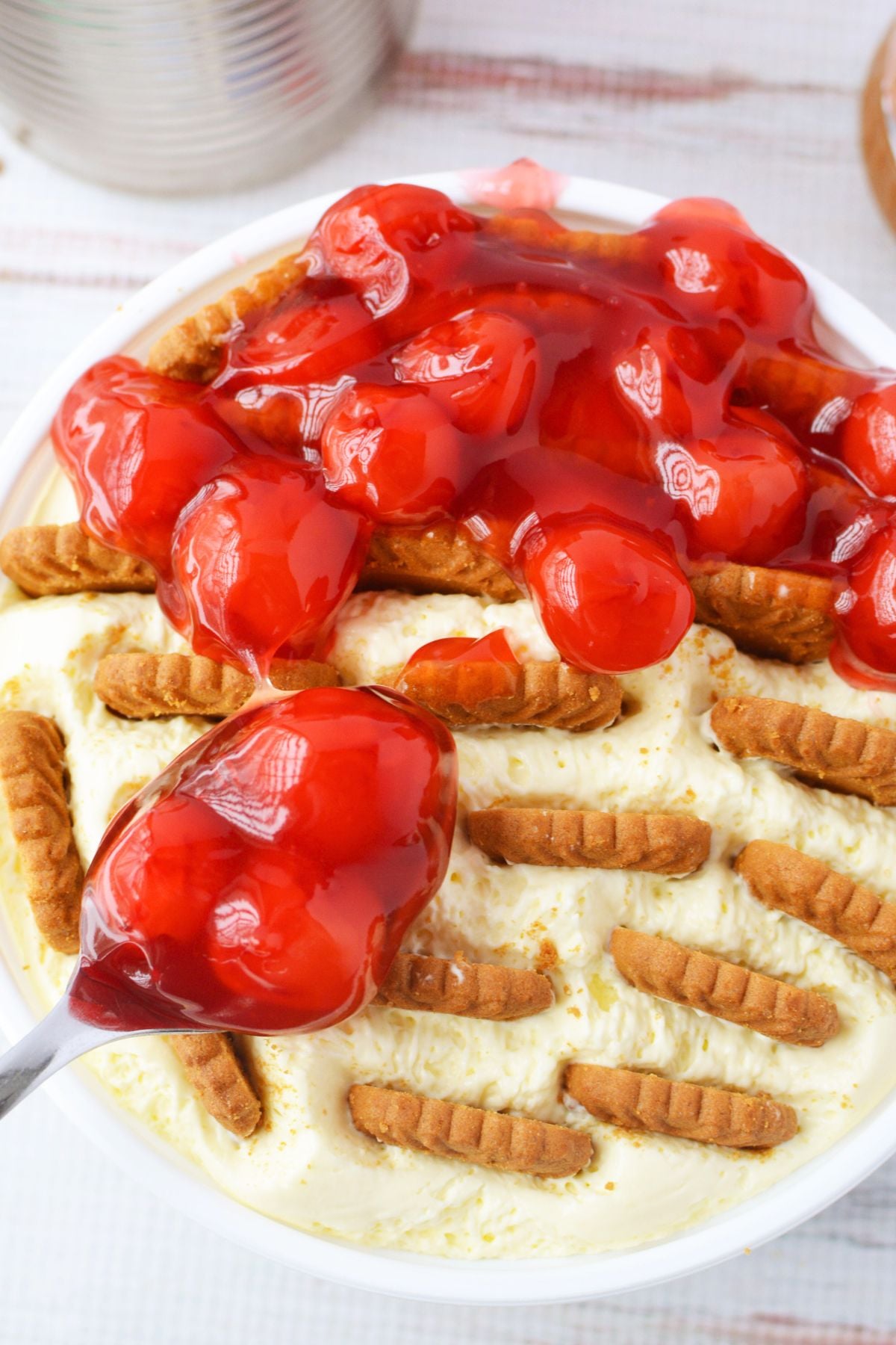 Spoon pouring cherry pie filling over creamy no bake cheesecake with Biscoff cookies