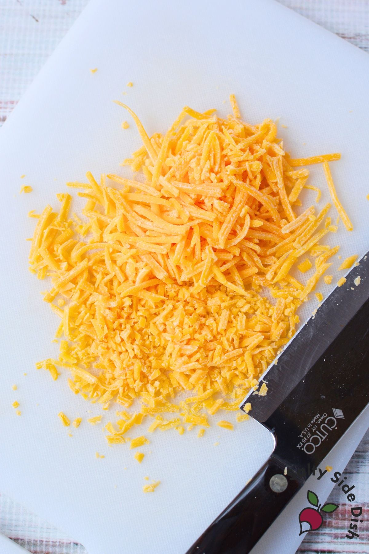 shredded cheddar cheese being chopped into smaller pieces on a white cutting board for cheeseball coating