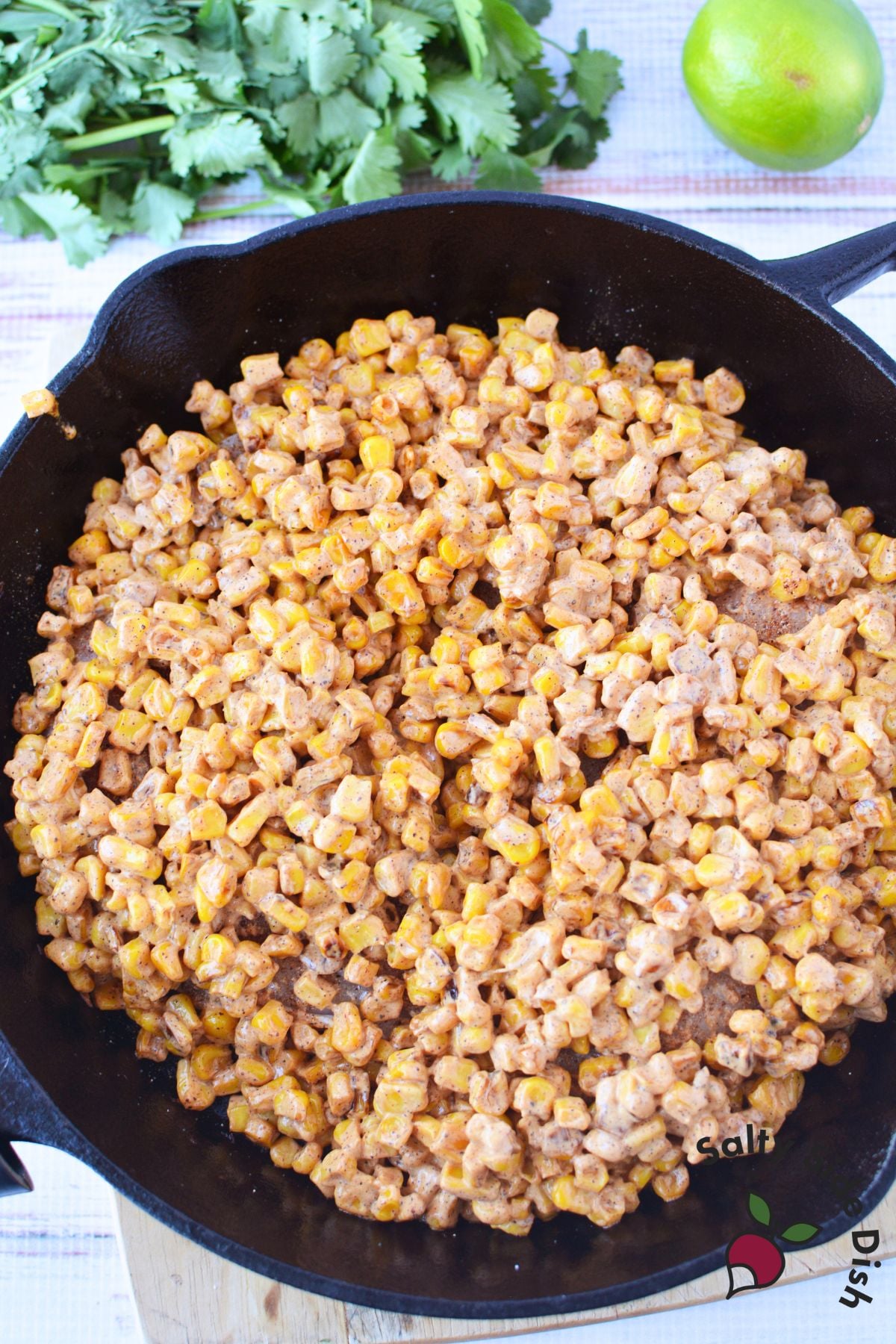 Charred corn mixed with creamy elote sauce in a cast iron skillet for street corn chicken bake