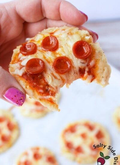 hand holding a cottage cheese mini pizza with a bite taken out, showing melted mozzarella and mini pepperoni