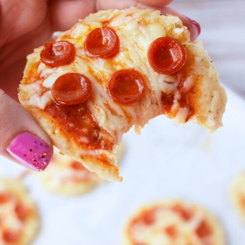 hand holding a cottage cheese mini pizza with a bite taken out, showing melted mozzarella and mini pepperoni