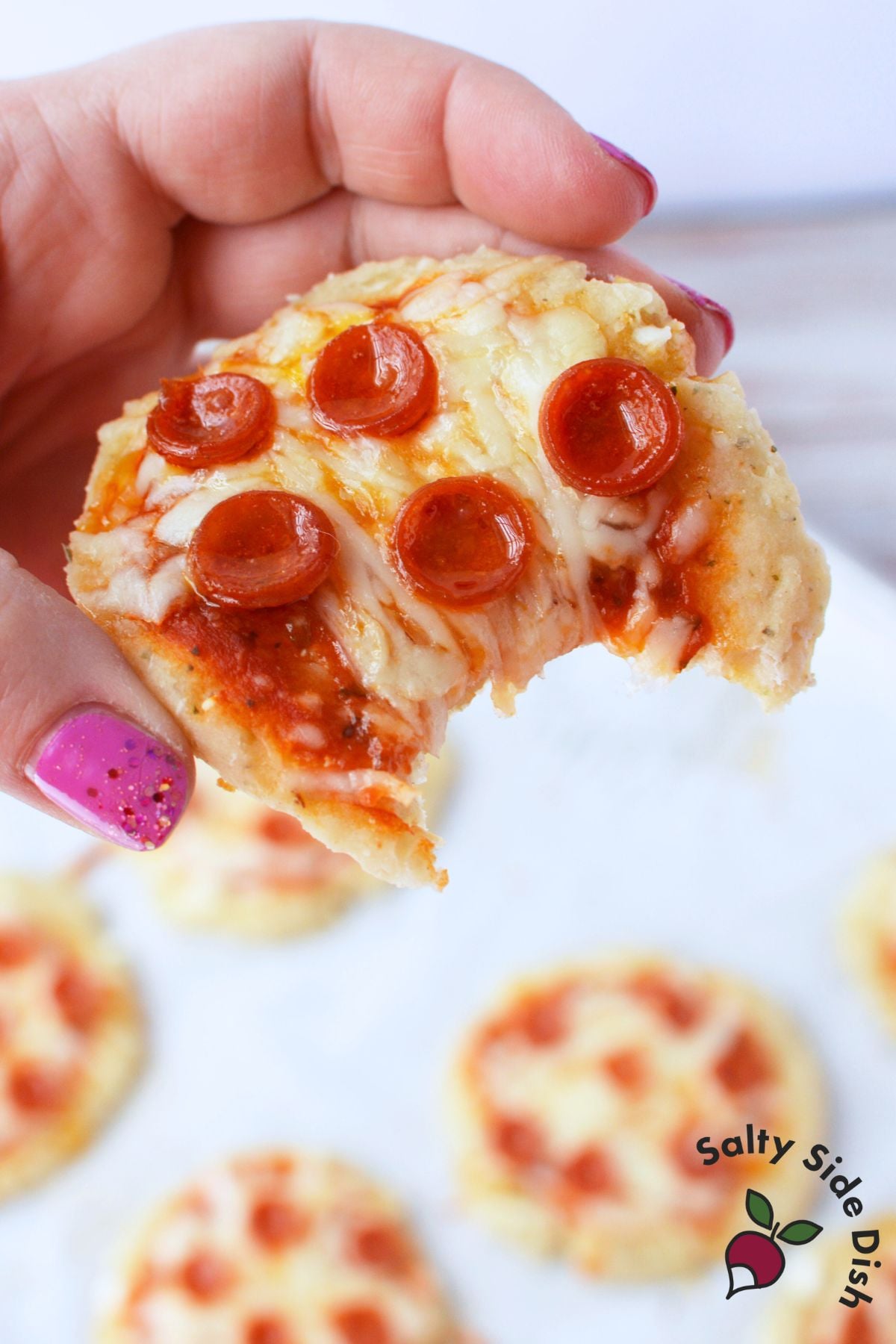 hand holding a cottage cheese mini pizza with a bite taken out, showing melted mozzarella and mini pepperoni