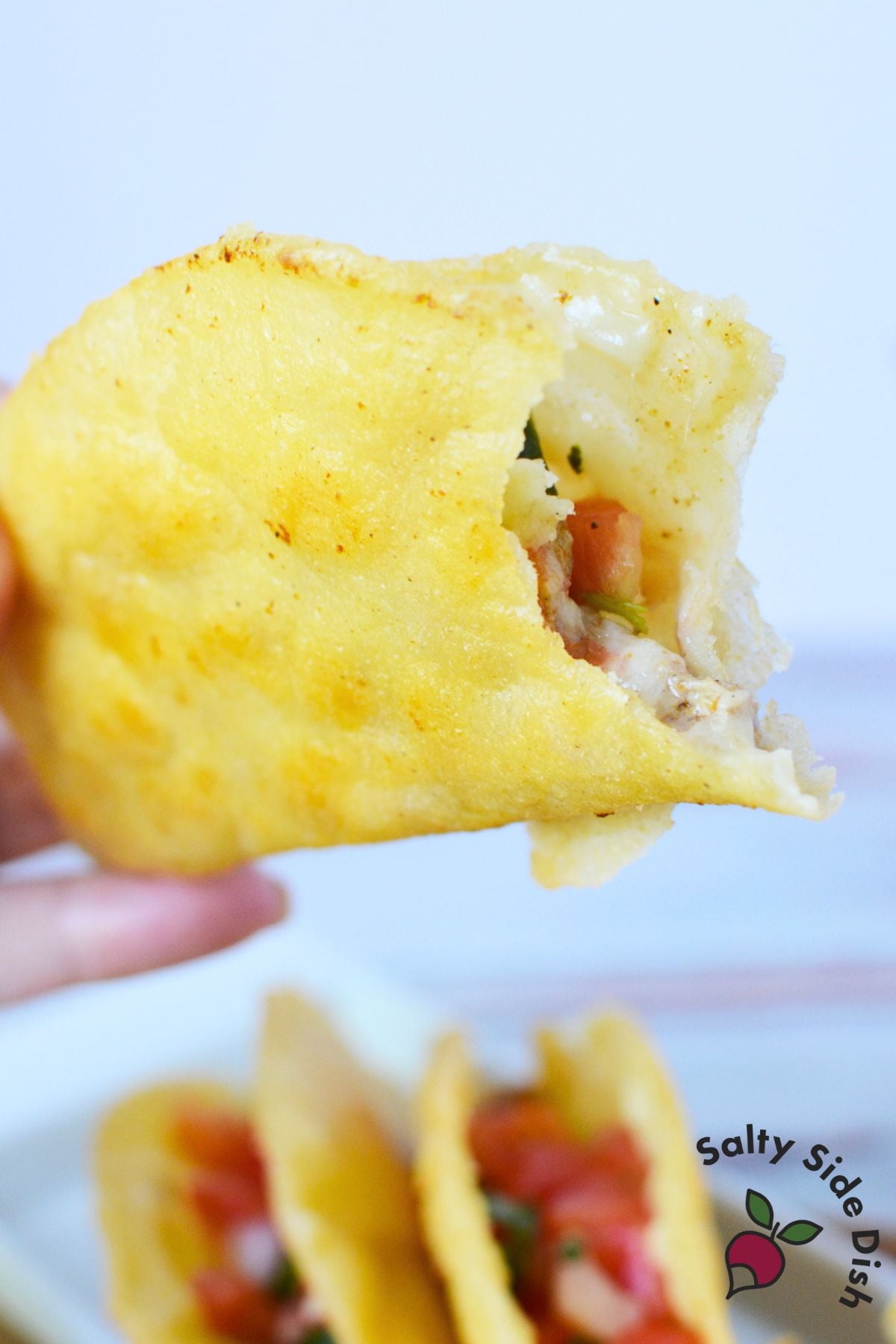 Hand holding crispy fried chicken taco showing melted cheese and chicken filling inside golden corn tortilla