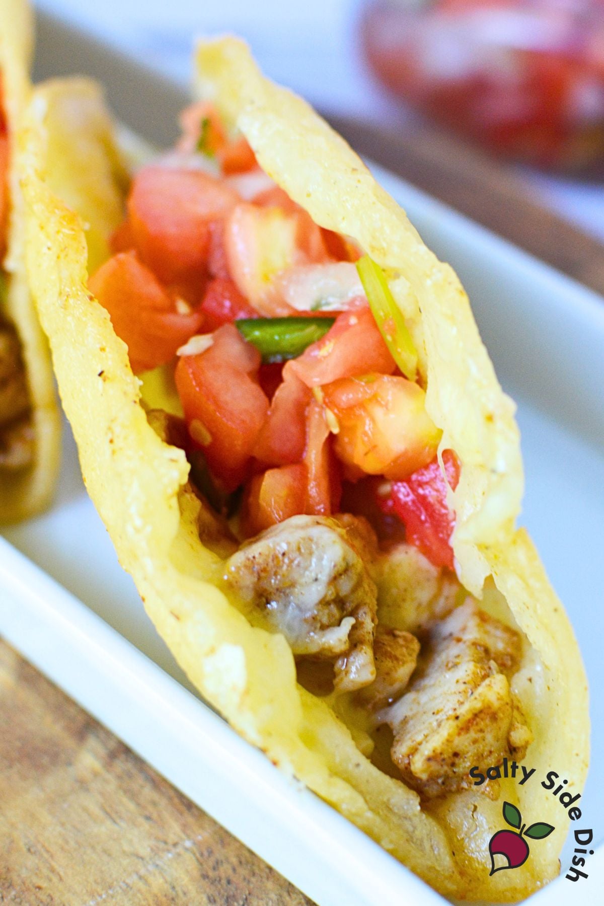 Open crispy chicken taco on white plate filled with seasoned chicken, cheese, and fresh pico de gallo