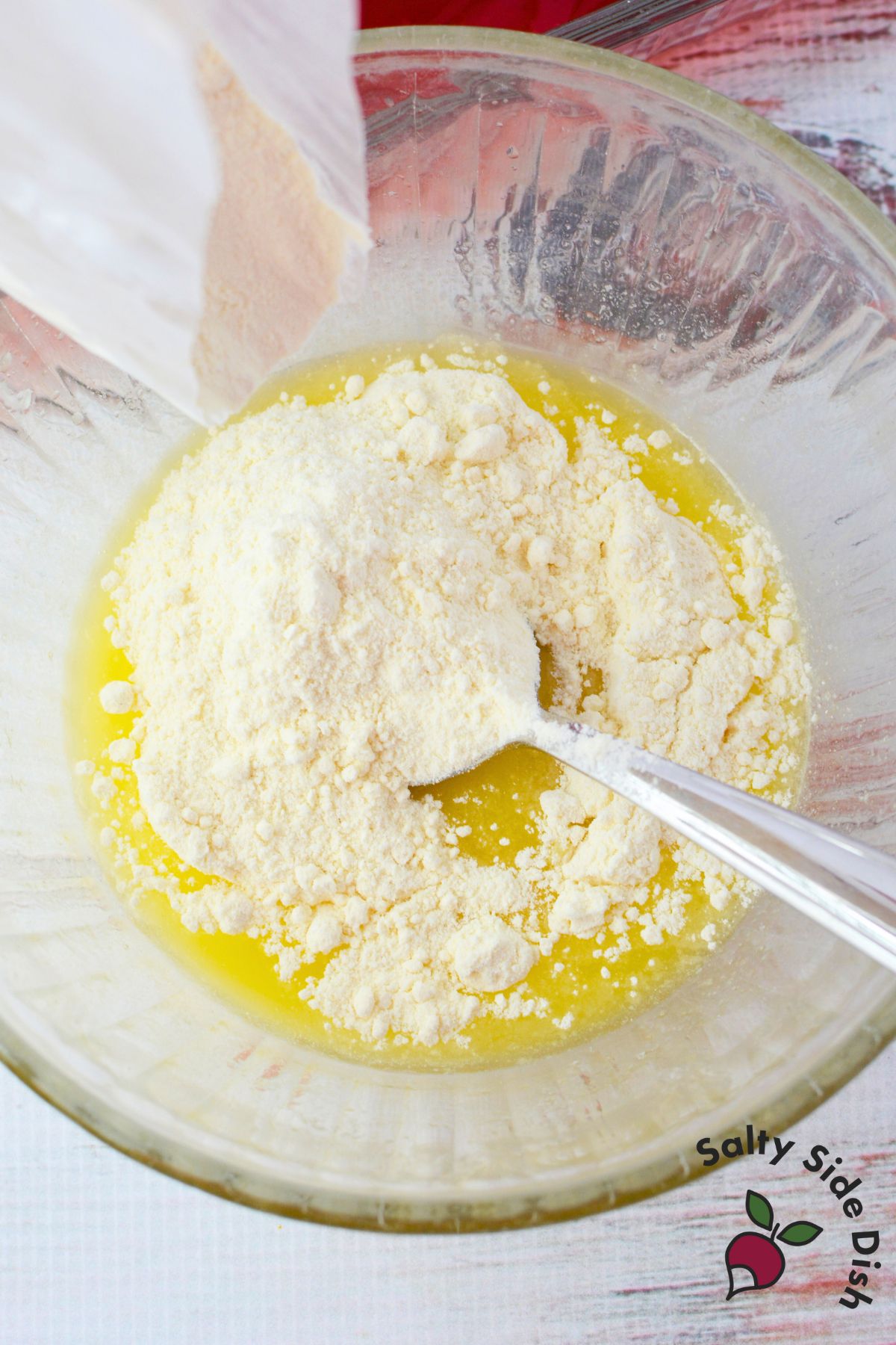 Lemon cake mix and melted butter being combined in a glass bowl with a spoon to make a crumbly dump cake topping
