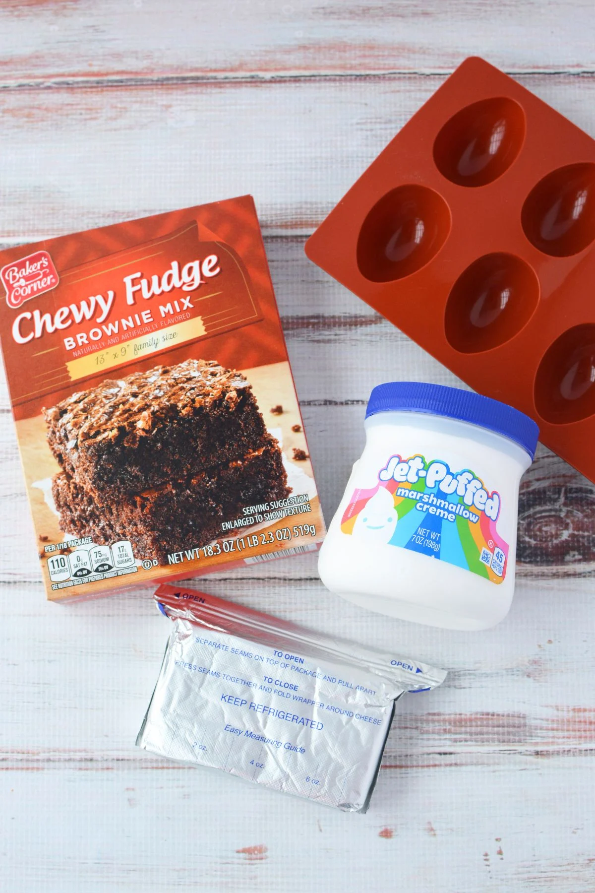 Ingredients for deviled brownies including brownie mix, cream cheese, marshmallow creme, and silicone egg molds