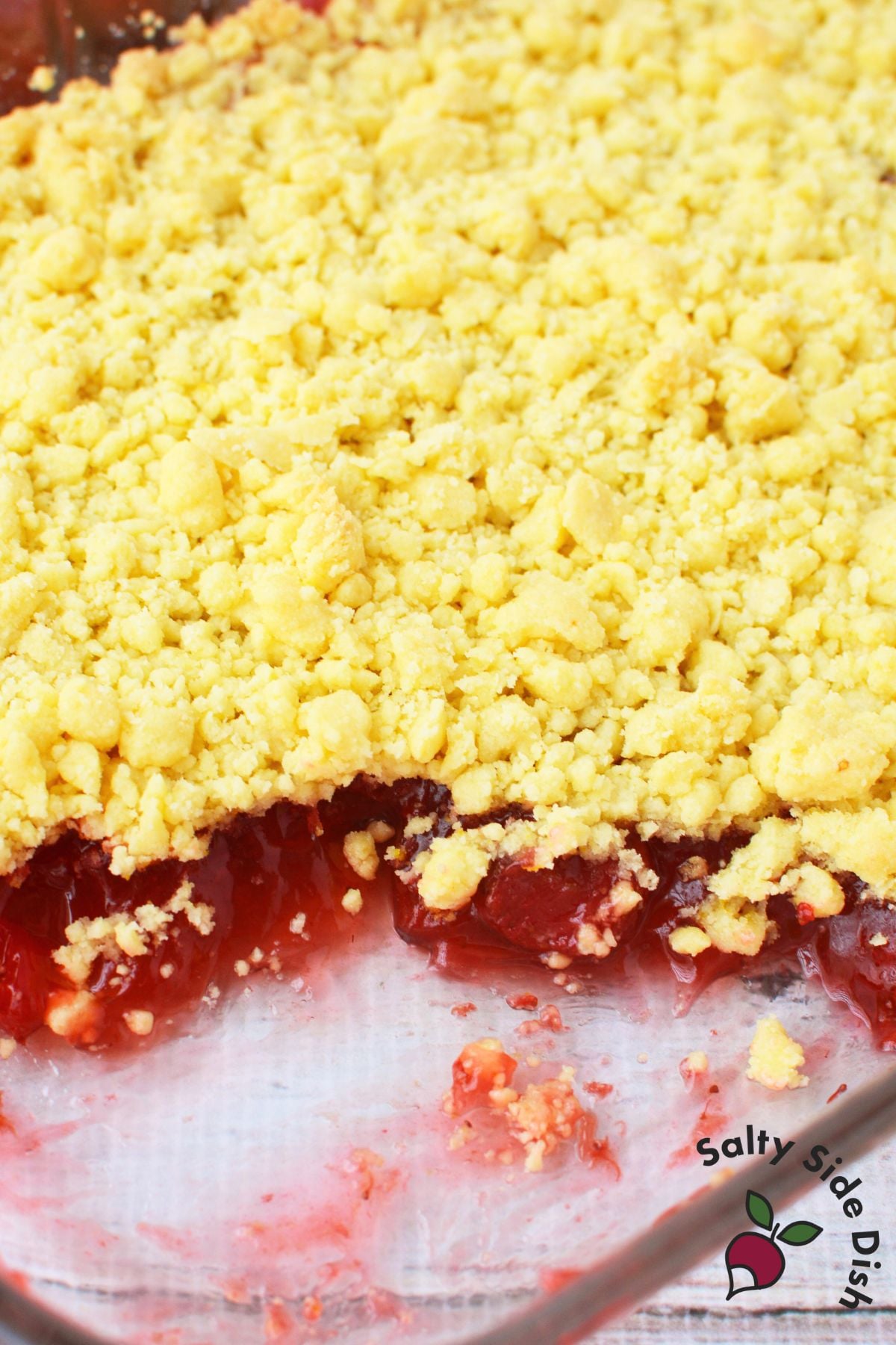 Unbaked strawberry lemon dump cake in a glass casserole dish showing the lemon cake mix crumb topping layered over strawberry pie filling